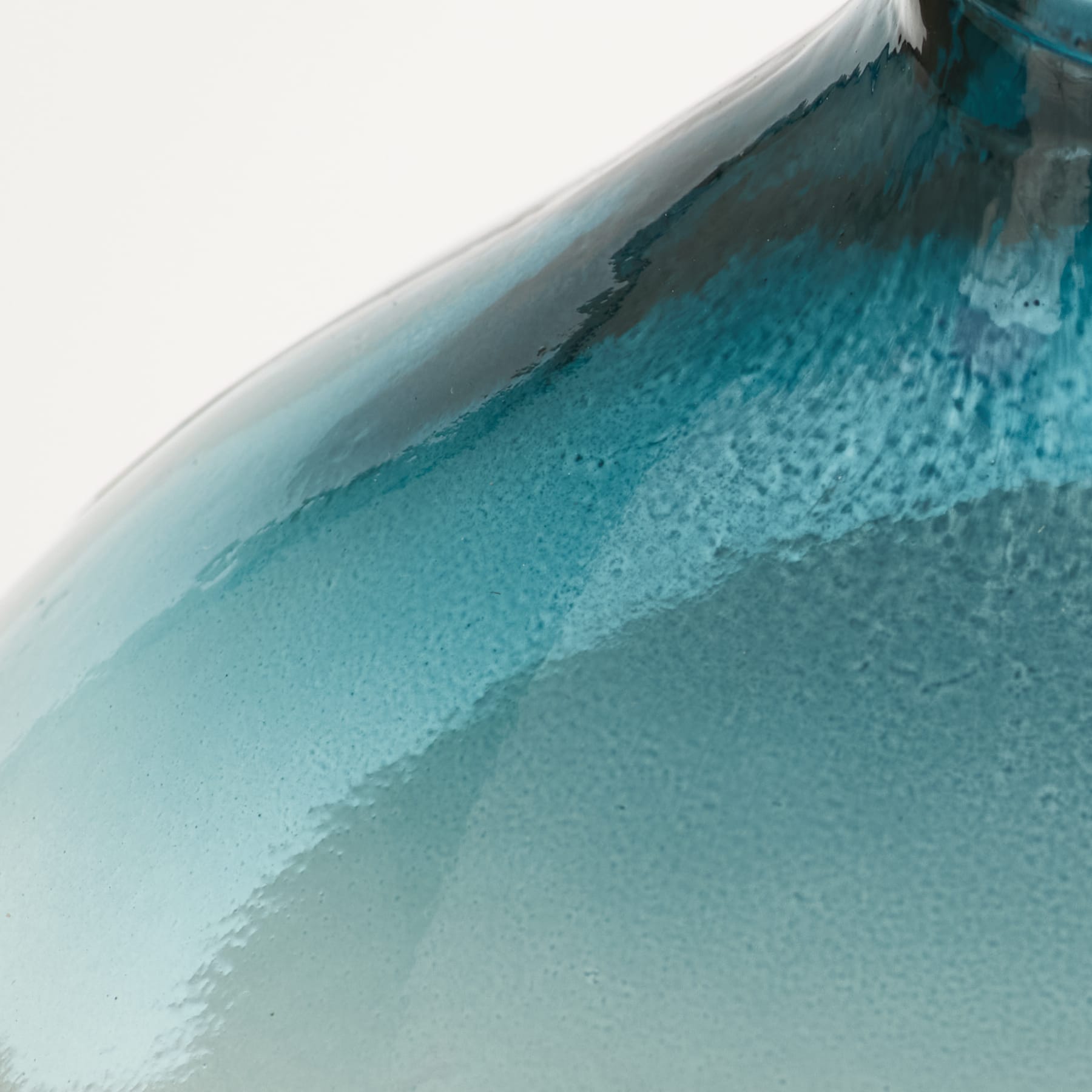 Eine Nahaufnahme einer strukturierten, blaugrünen Glasvase mit glatter, reflektierender Oberfläche geht in einen verschwommenen weißen Hintergrund über.