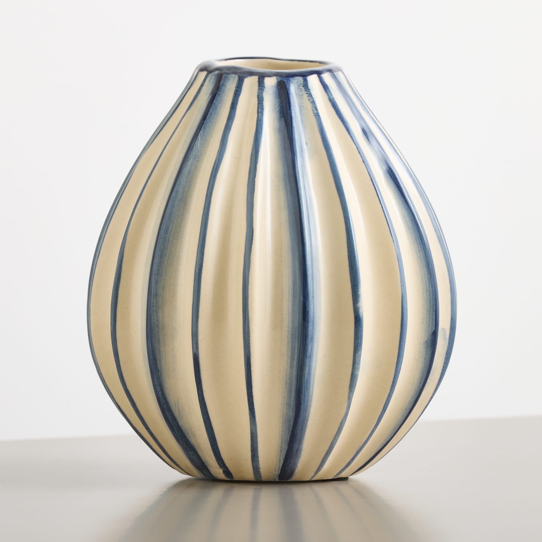 Eine cremefarbene Vase mit vertikalen blauen Streifen steht auf einer grauen Fläche vor einem schlichten weißen Hintergrund.