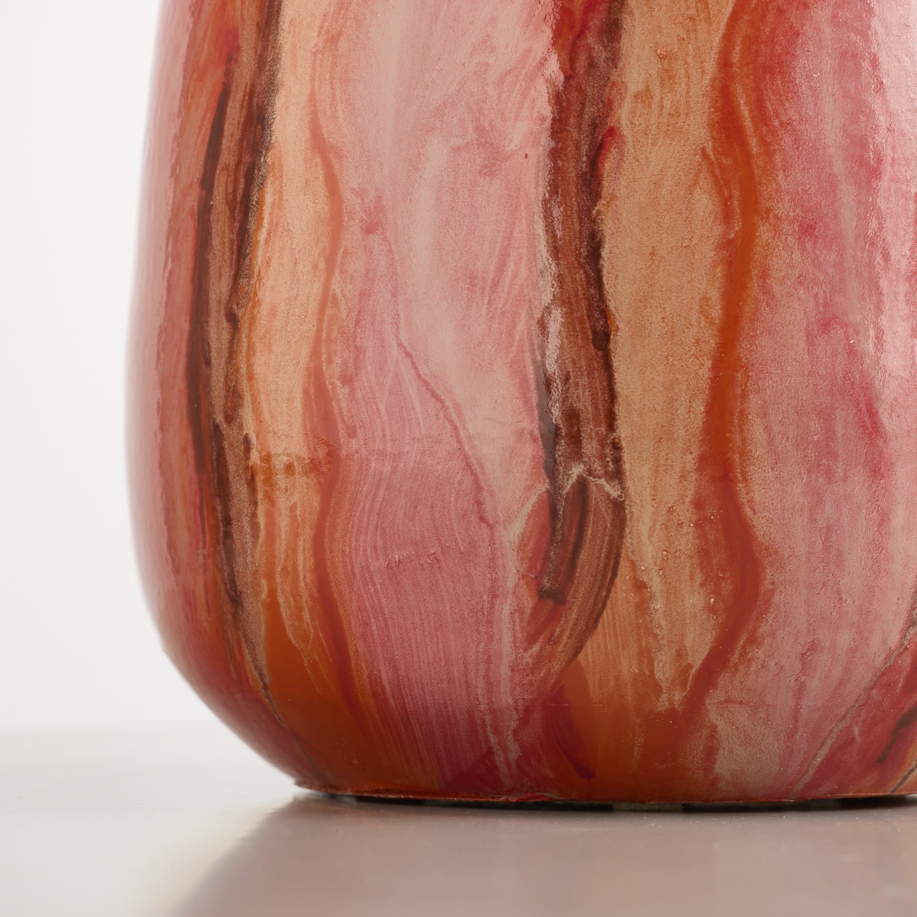 Nahaufnahme einer Vase mit wirbelnden rosa und orangen Mustern auf einer weißen Oberfläche vor einem schlichten weißen Hintergrund.