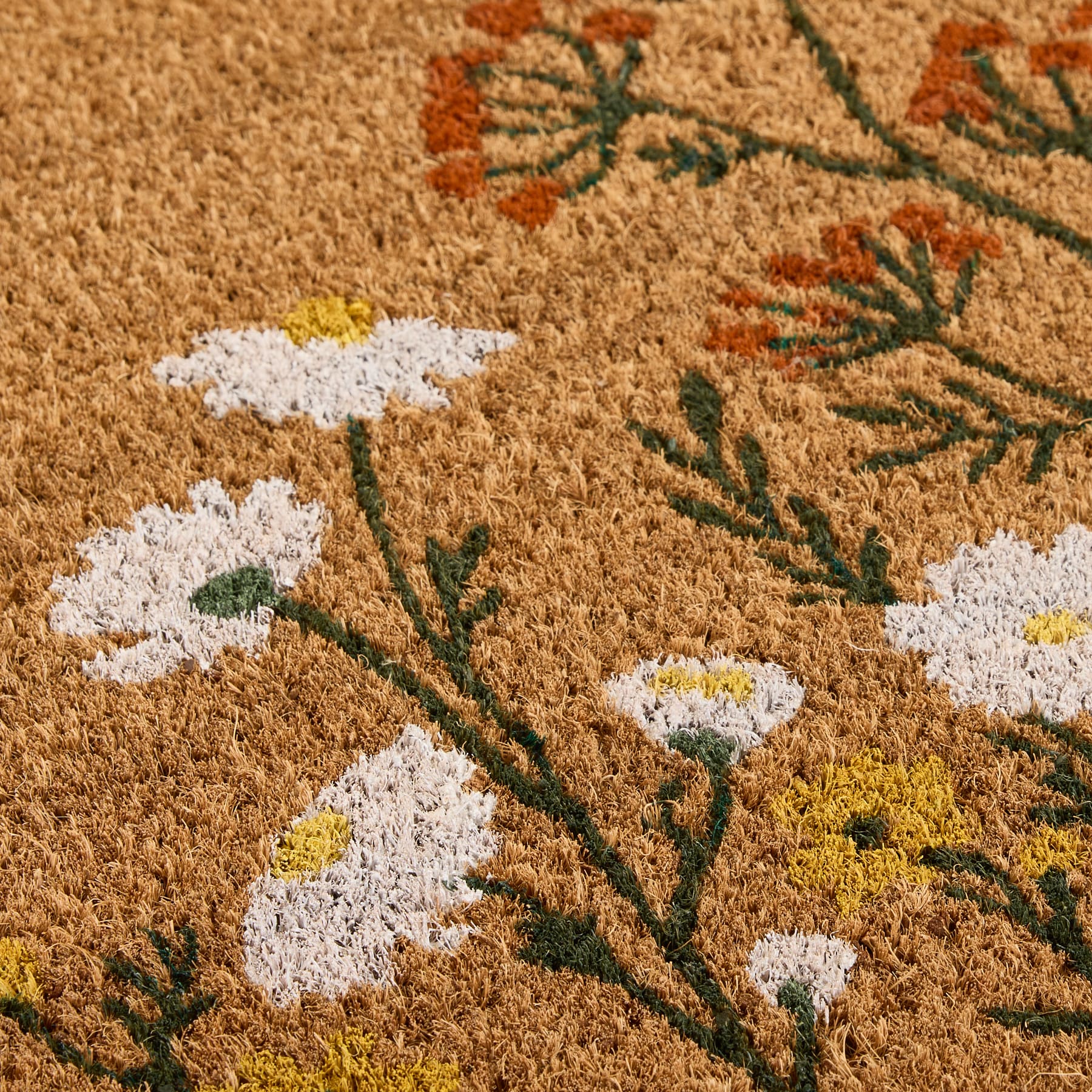 Nahaufnahme einer Kokosfaser-Fußmatte mit einem floralen Muster aus weißen Gänseblümchen und orangefarbenen Wildblumen.