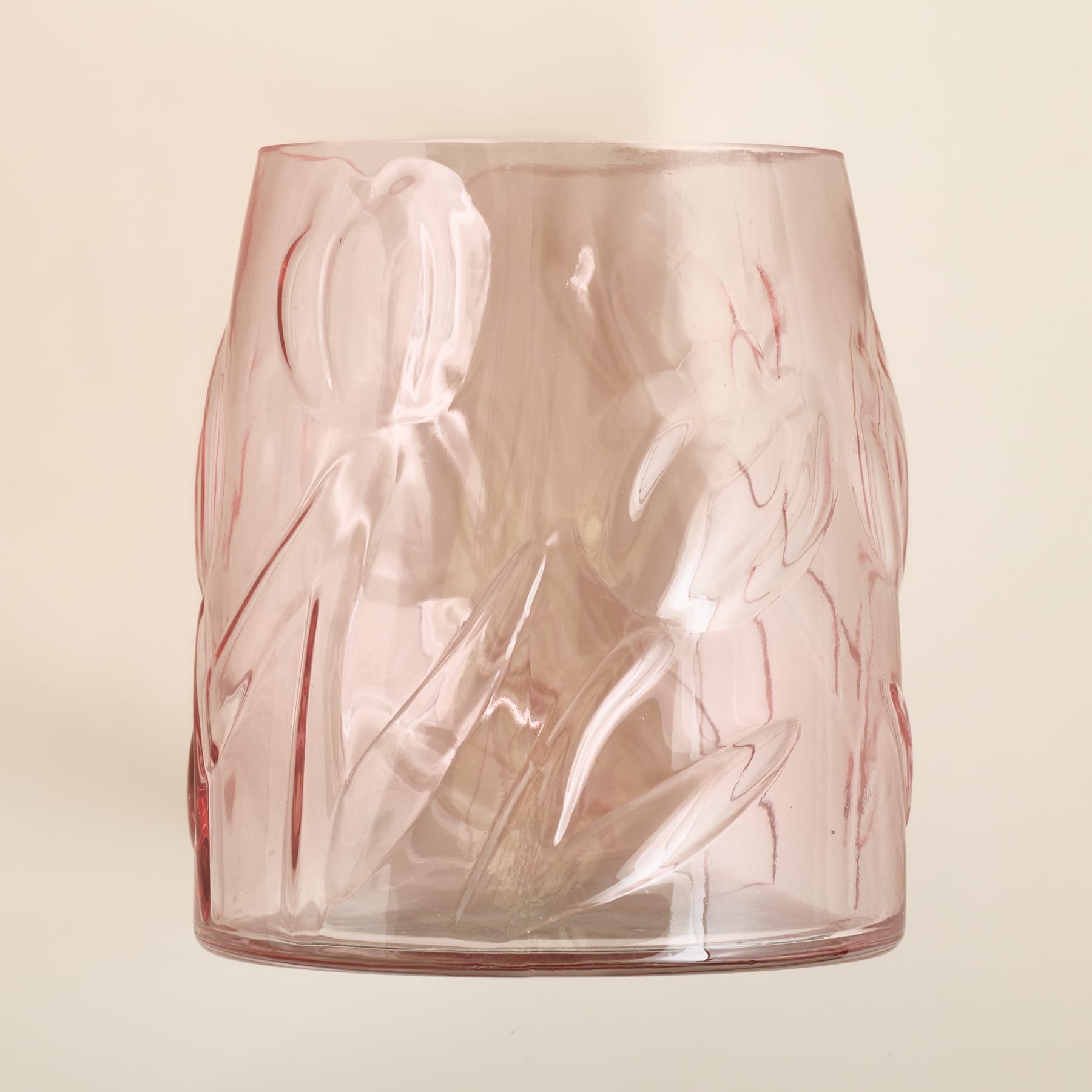 Eine durchscheinende rosa Glasvase mit geprägten Blumenmotiven steht vor einem sanften, neutralen Hintergrund.