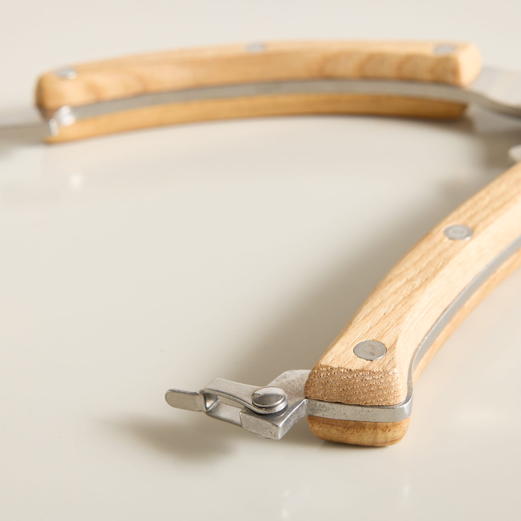 Zwei Küchenmesser mit Holzgriffen und Metallelementen liegen auf einer hellen Oberfläche, wobei sich ein Messer im Vordergrund und das andere im Hintergrund verschwommen befindet.