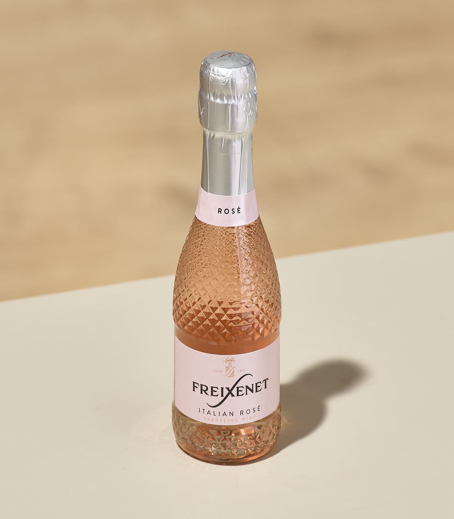 Eine rosafarbene, prickelnde Flasche italienischen Roséweins steht auf einer Holzoberfläche vor einem hellen Hintergrund.