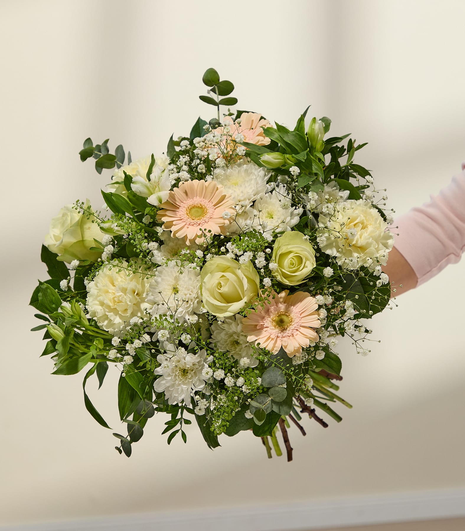 Ein lebhafter Strauß aus weißen und hellrosa Blumen, darunter Rosen, Gänseblümchen und anderes Grün, füllt das Bild vor einem schlichten weißen Hintergrund.