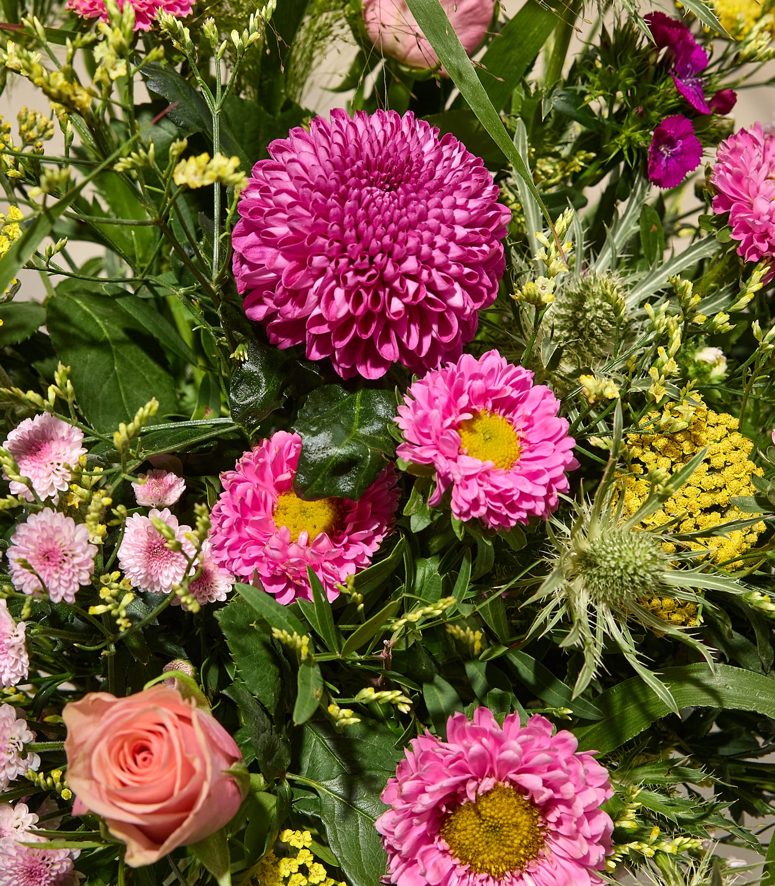 Ein leuchtender Strauß aus rosa und pfirsichfarbenen Blumen, darunter eine große Chrysantheme und Rosen, hebt sich von einem weichen, verschwommenen Hintergrund ab. (Beschreibungstext KI-generiert)
