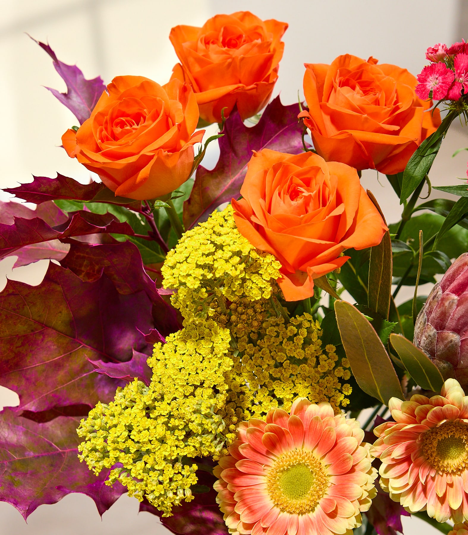 Ein farbenfroher Blumenstrauß mit rosa Rosen, Nelken und Chrysanthemen wird von einer Person in einem schwarzen Hemd vor einem schlichten weißen Hintergrund gehalten. (Beschreibungstext KI-generiert)