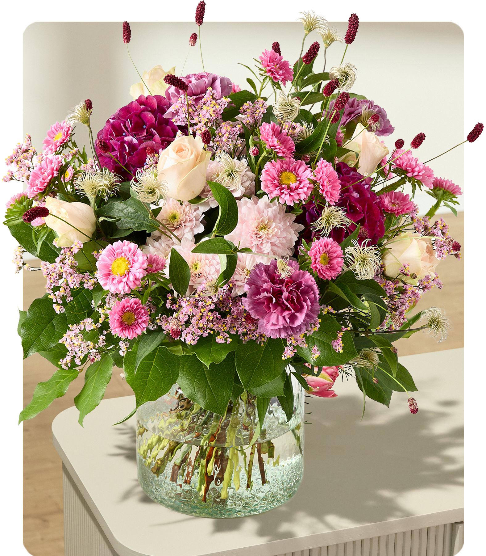 Ein leuchtender Strauß rosa und weißer Blumen füllt eine durchsichtige Glasvase auf hellem Untergrund vor einem weichen, verschwommenen Hintergrund. (Beschreibungstext KI-generiert)
