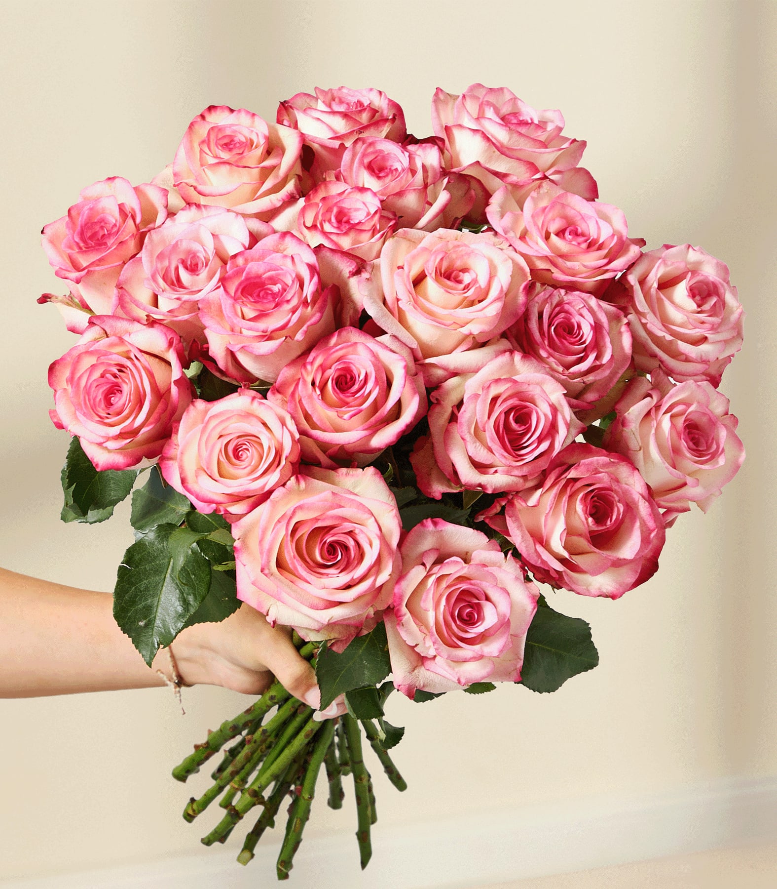 Ein wunderschöner Strauß leuchtend pinkfarbener Rosen in einer Glasvase steht auf einer hellen Fläche vor einer schlichten weißen Wand.