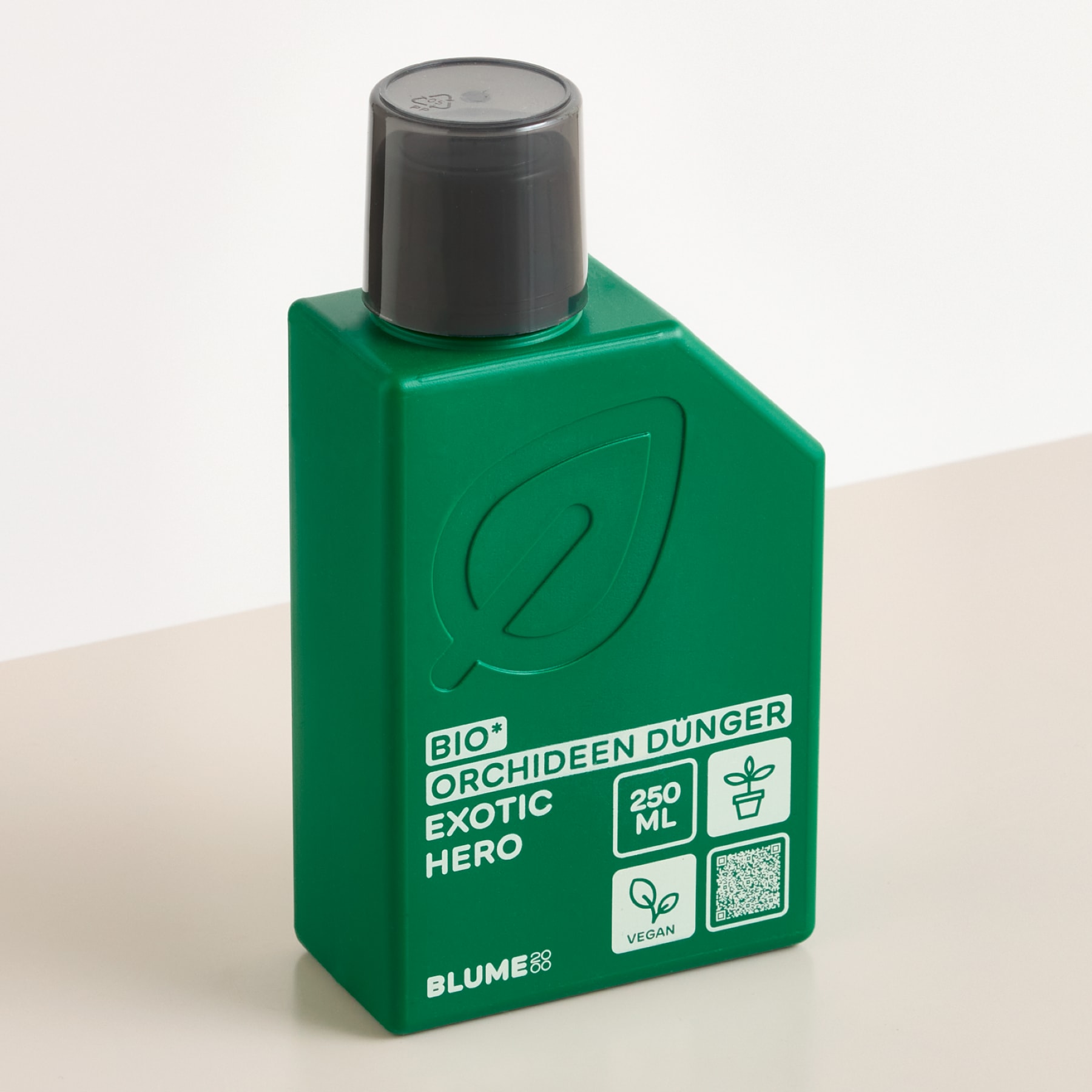Vor einer blühenden rosa Orchidee steht eine grüne Flasche Orchideendünger vor einem neutralen Hintergrund.