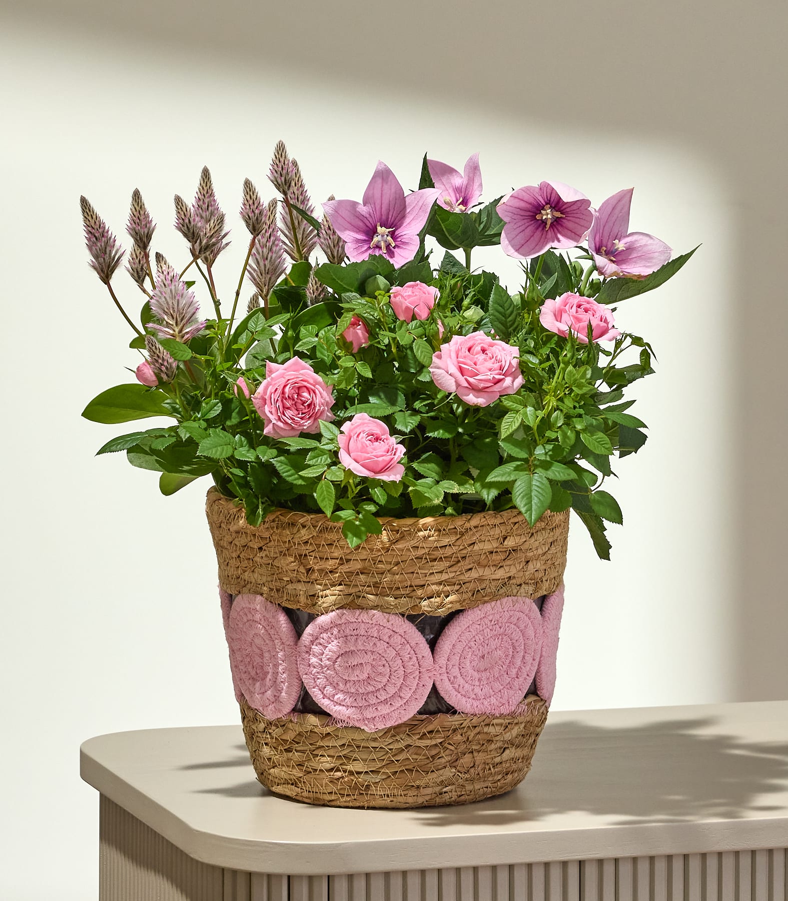 Ein lebhafter Strauß aus rosa Rosen und zarten rosa und weißen Blüten mit grünem Laub füllt das Bild und schafft eine üppige und optisch ansprechende Szene.