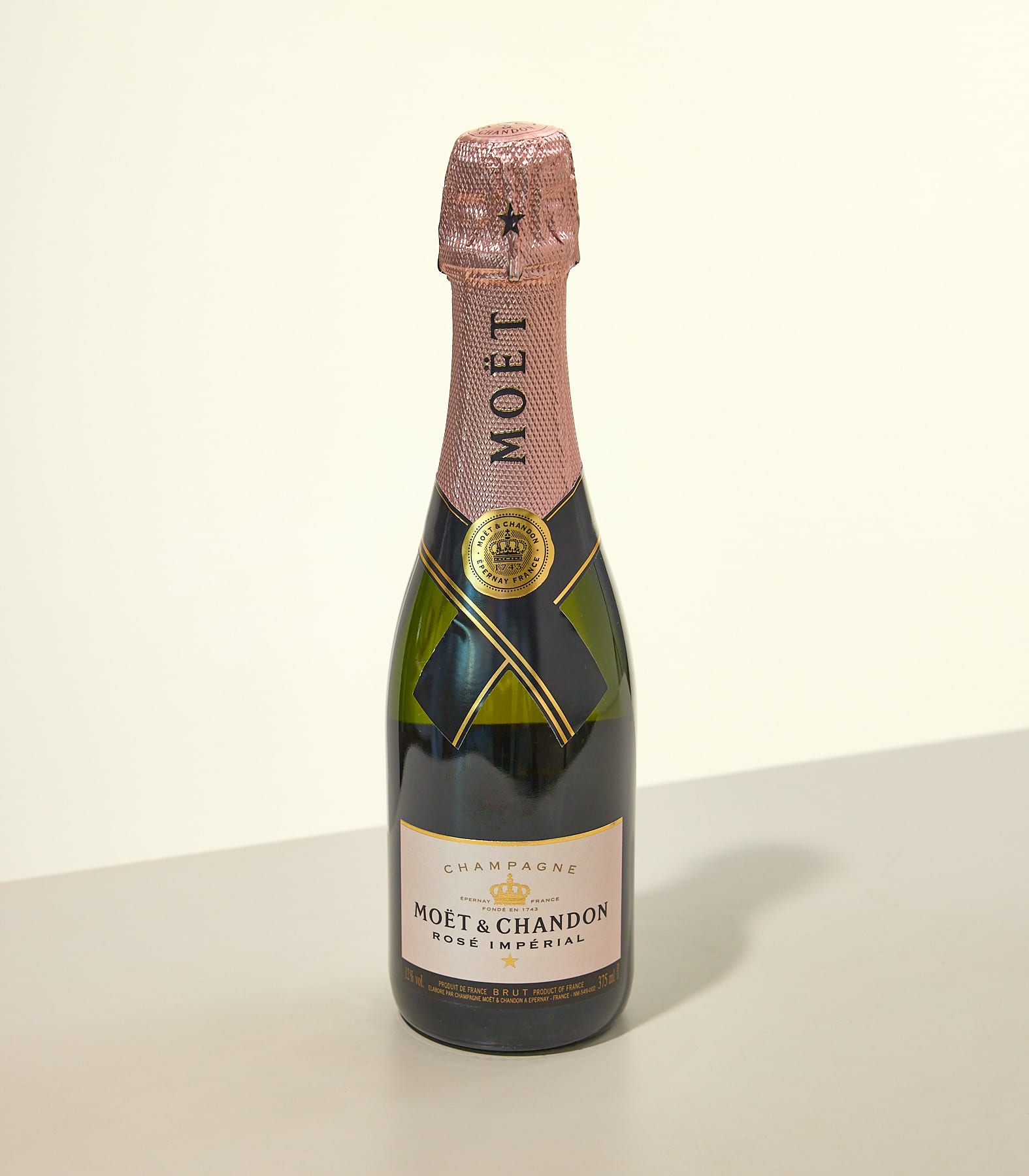 Eine Flasche Moët & Chandon Champagner mit rosa Etikett steht auf einer beigen Oberfläche vor einem schlichten weißen Hintergrund.