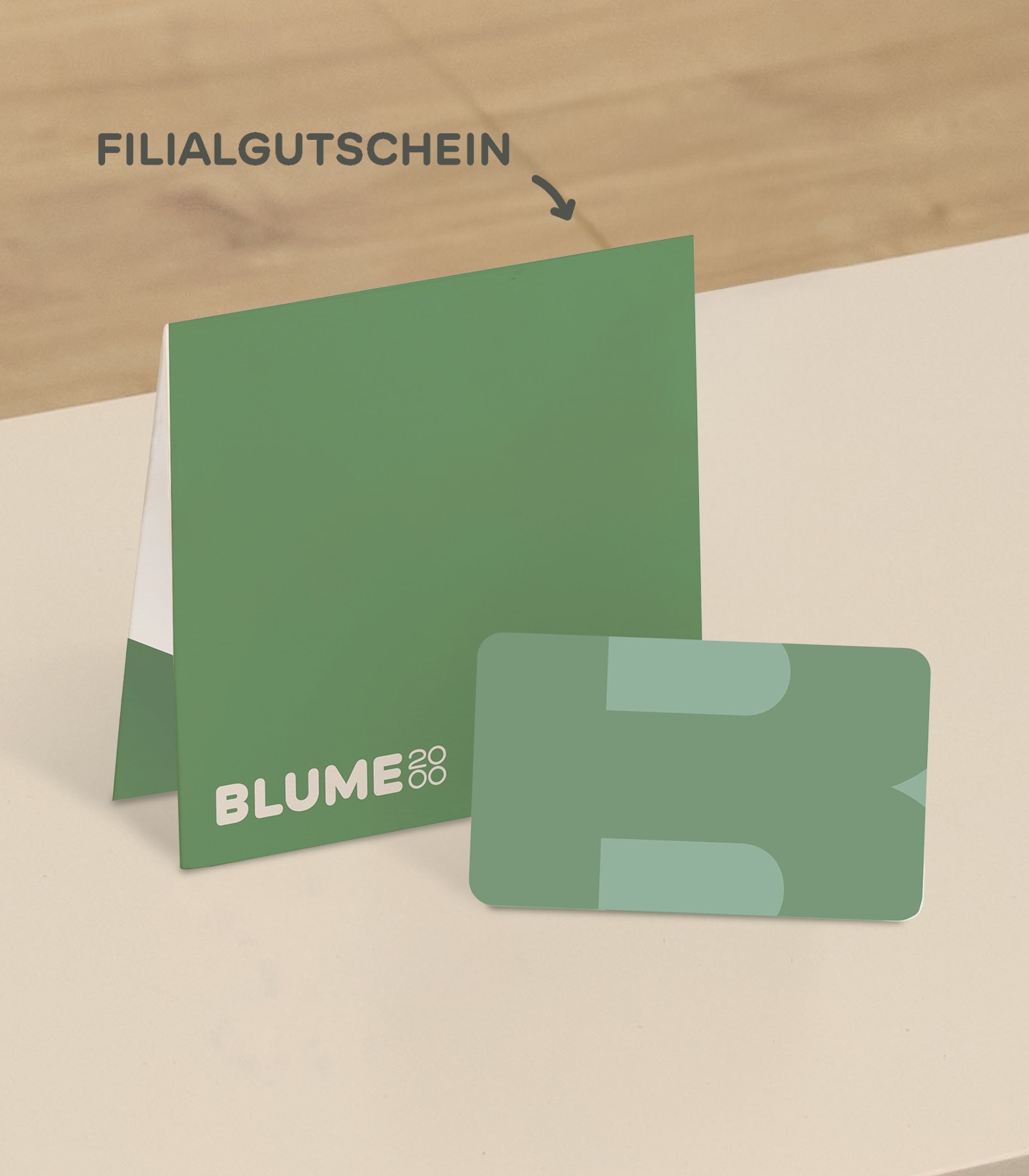 Eine grüne Geschenkkarte und eine dazu passende Faltkarte mit dem Text "FILIALGUTSCHEIN" und "BLUME88" liegen auf einer hellen Oberfläche mit Holzuntergrund. (Beschreibungstext KI-generiert)