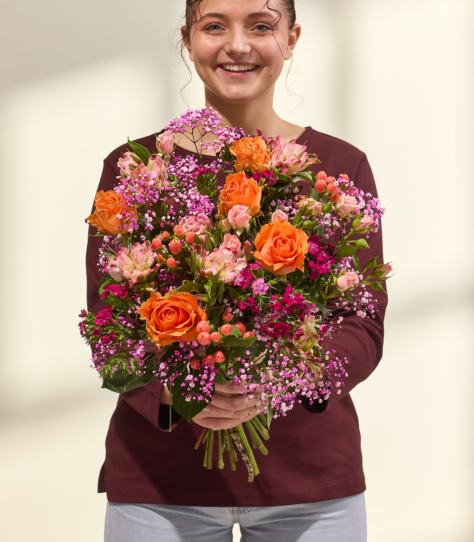 Ein lebhafter Blumenstrauß aus roten, rosa und orangen Blüten, darunter Rosen, Alstroemerien und andere Blüten, füllt das Bild vor einem schlichten weißen Hintergrund. (Beschreibungstext KI-generiert)