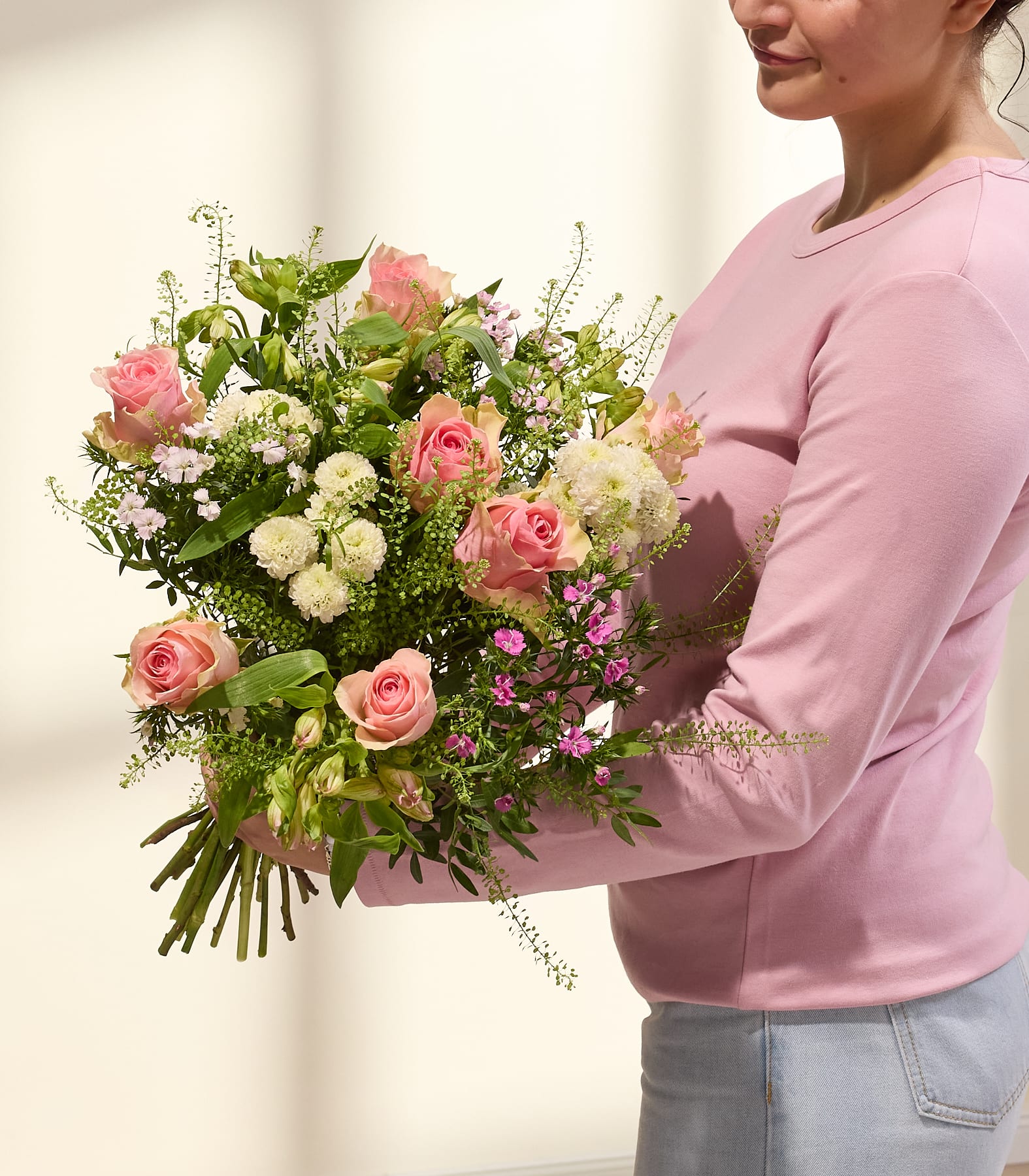 Ein wunderschöner Strauß aus rosa Rosen und anderen leuchtenden Blumen, arrangiert in einer Glasvase, steht auf einem Holztisch vor einem schlichten Hintergrund. (Beschreibungstext KI-generiert)
