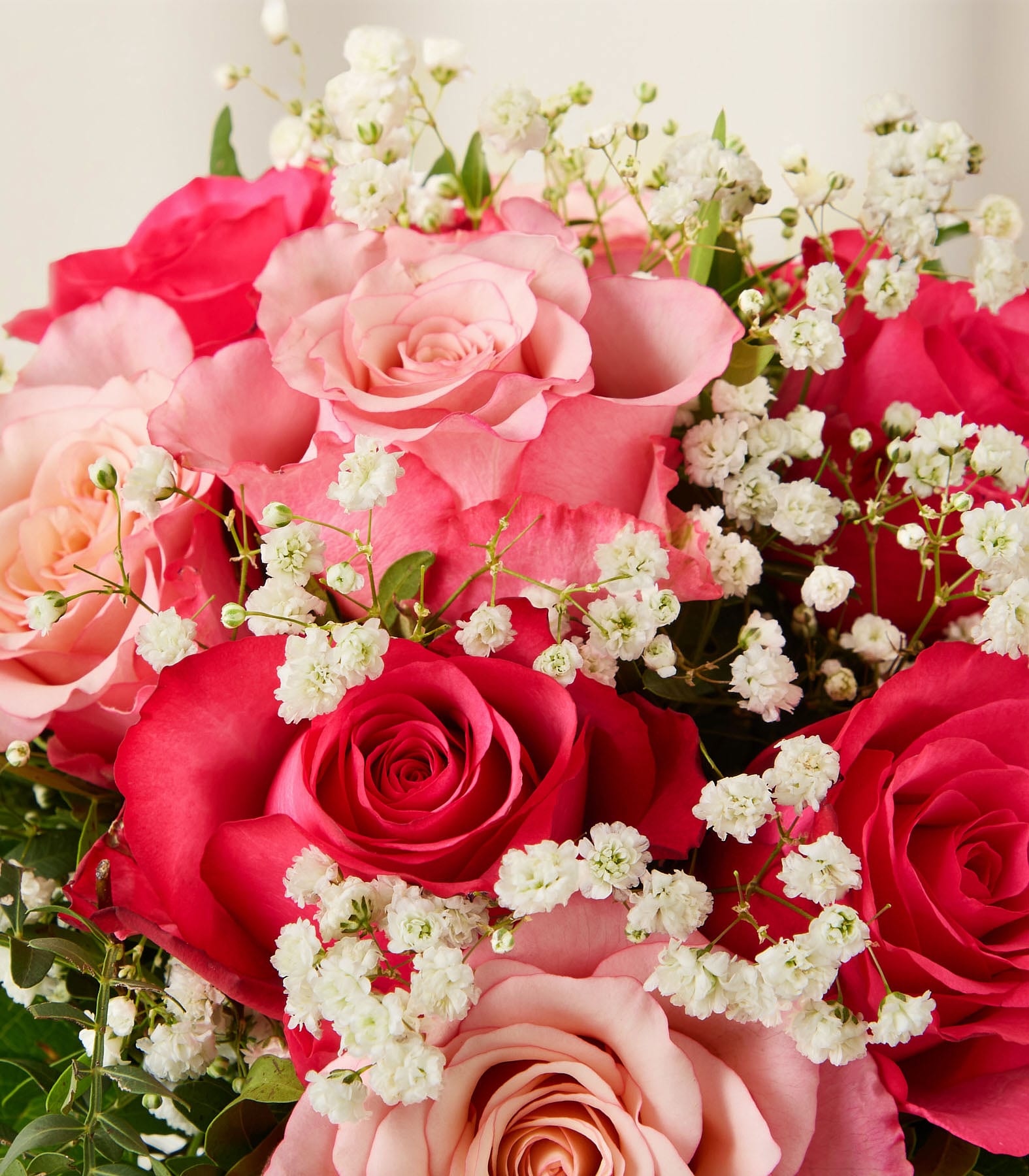 Eine Hand hält einen wunderschönen Strauß aus leuchtend pinken und roten Rosen, Schleierkraut und anderen zarten Blumen, die in einer Glasvase vor einem schlichten, hellen Hintergrund arrangiert sind. (Beschreibungstext KI-generiert)