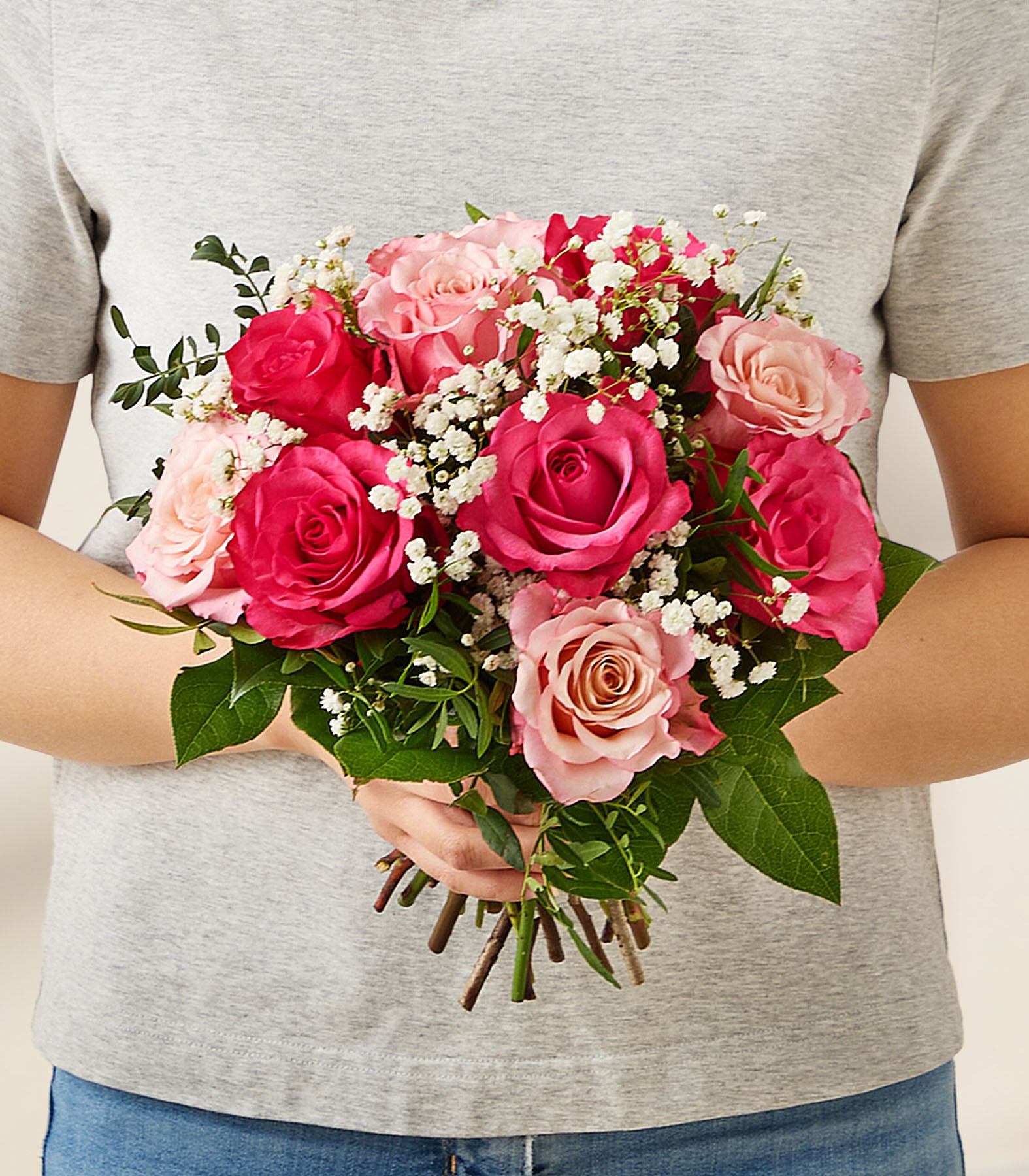 Ein Strauß aus leuchtend roten Rosen, zarten rosa Nelken und kleinen weißen Blüten, arrangiert in einer Glasvase, steht auf einer schlichten, hellen Oberfläche. (Beschreibungstext KI-generiert)