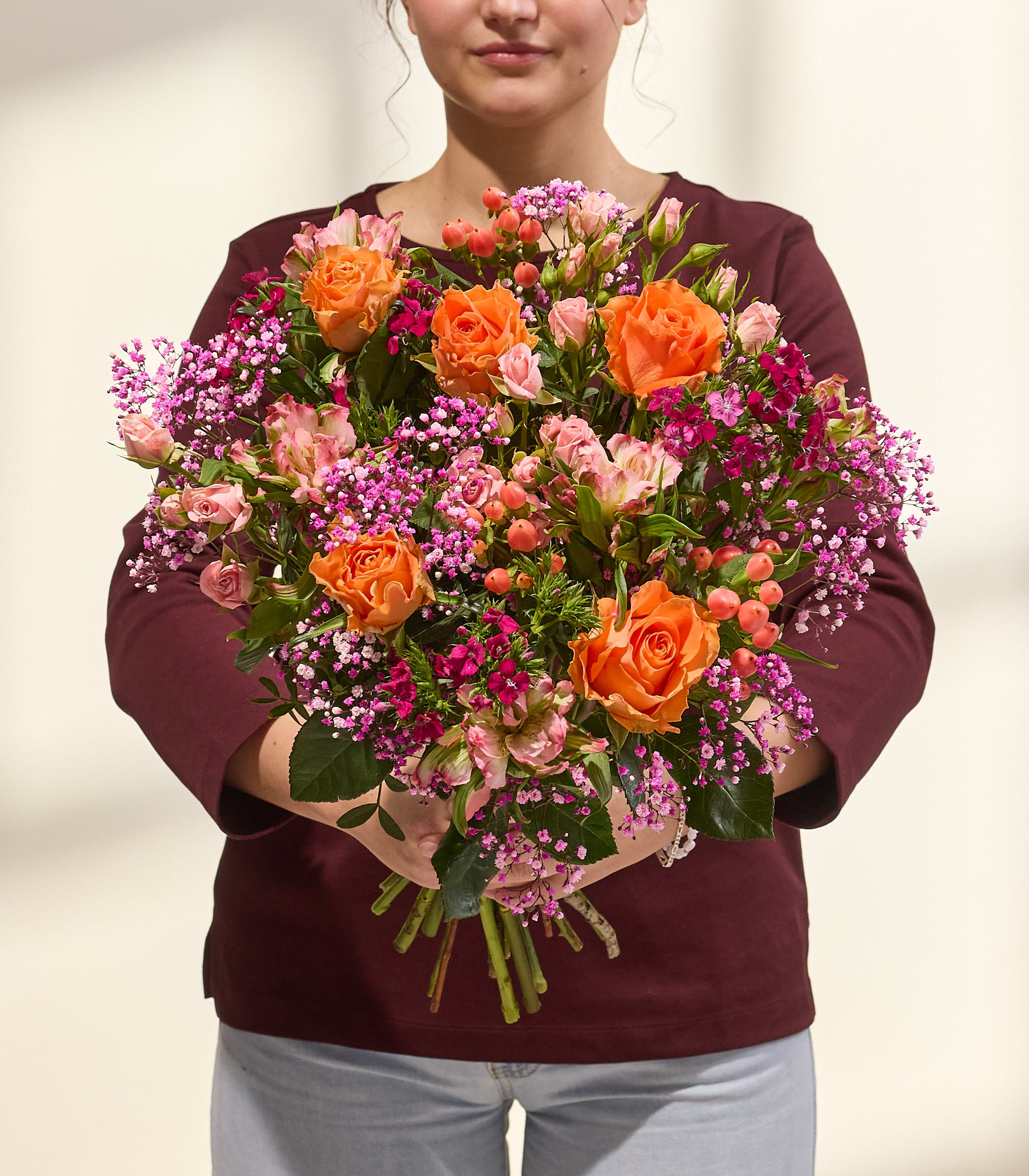 Ein farbenfroher Blumenstrauß mit Rosen, Dahlien und anderen Blüten wird von einer Person in einem schwarzen Hemd vor einem schlichten weißen Hintergrund gehalten. (Beschreibungstext KI-generiert)