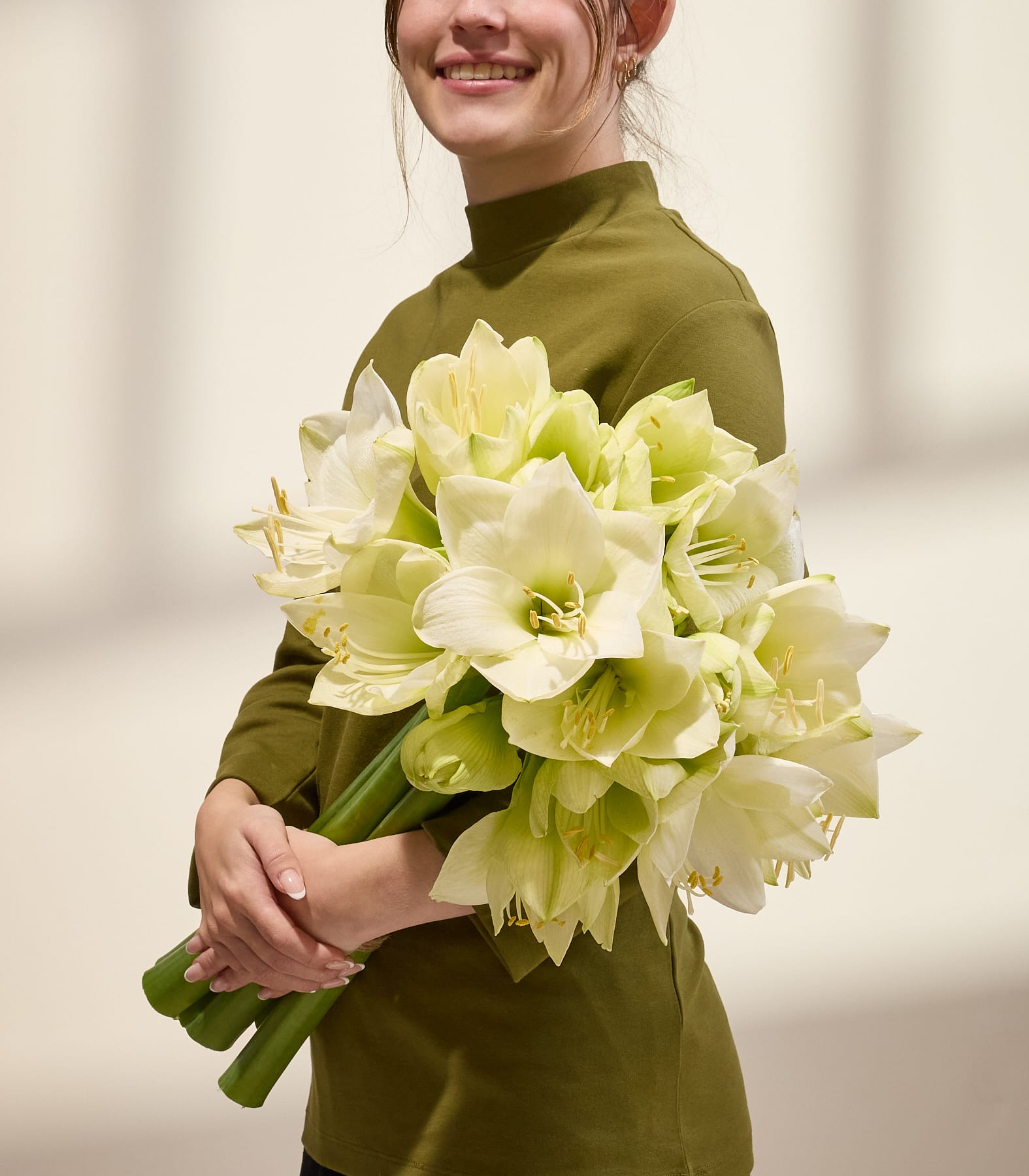 Ein Strauß leuchtend hellgrüner Dahlienblüten in den Händen einer Person vor einem schlichten, hellen Hintergrund. (Beschreibungstext KI-generiert)