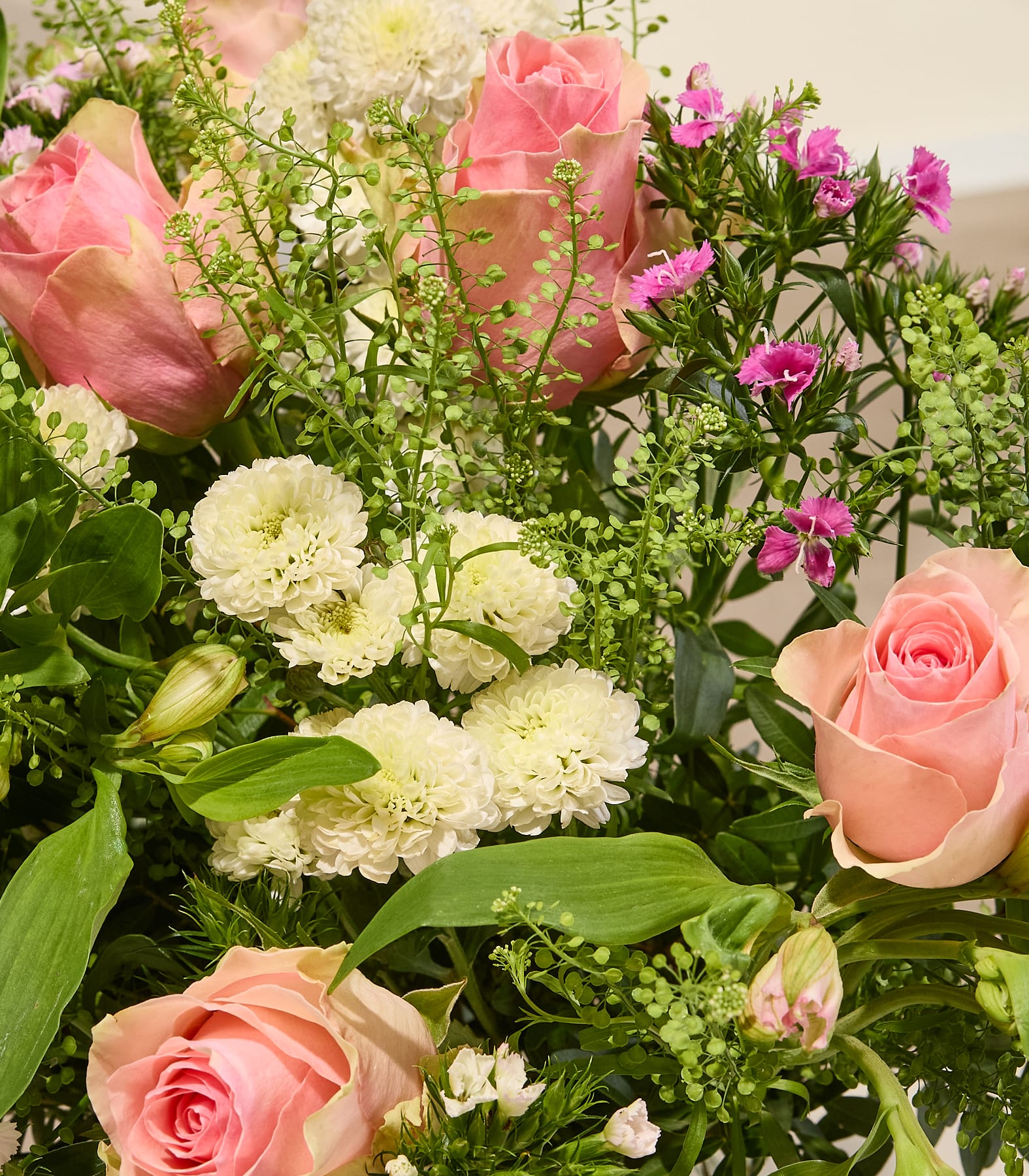 Ein lebhafter Strauß aus rosa und weißen Blumen, darunter Rosen und Nelken, arrangiert mit üppigem Grün vor einem schlichten weißen Hintergrund. (Beschreibungstext KI-generiert)