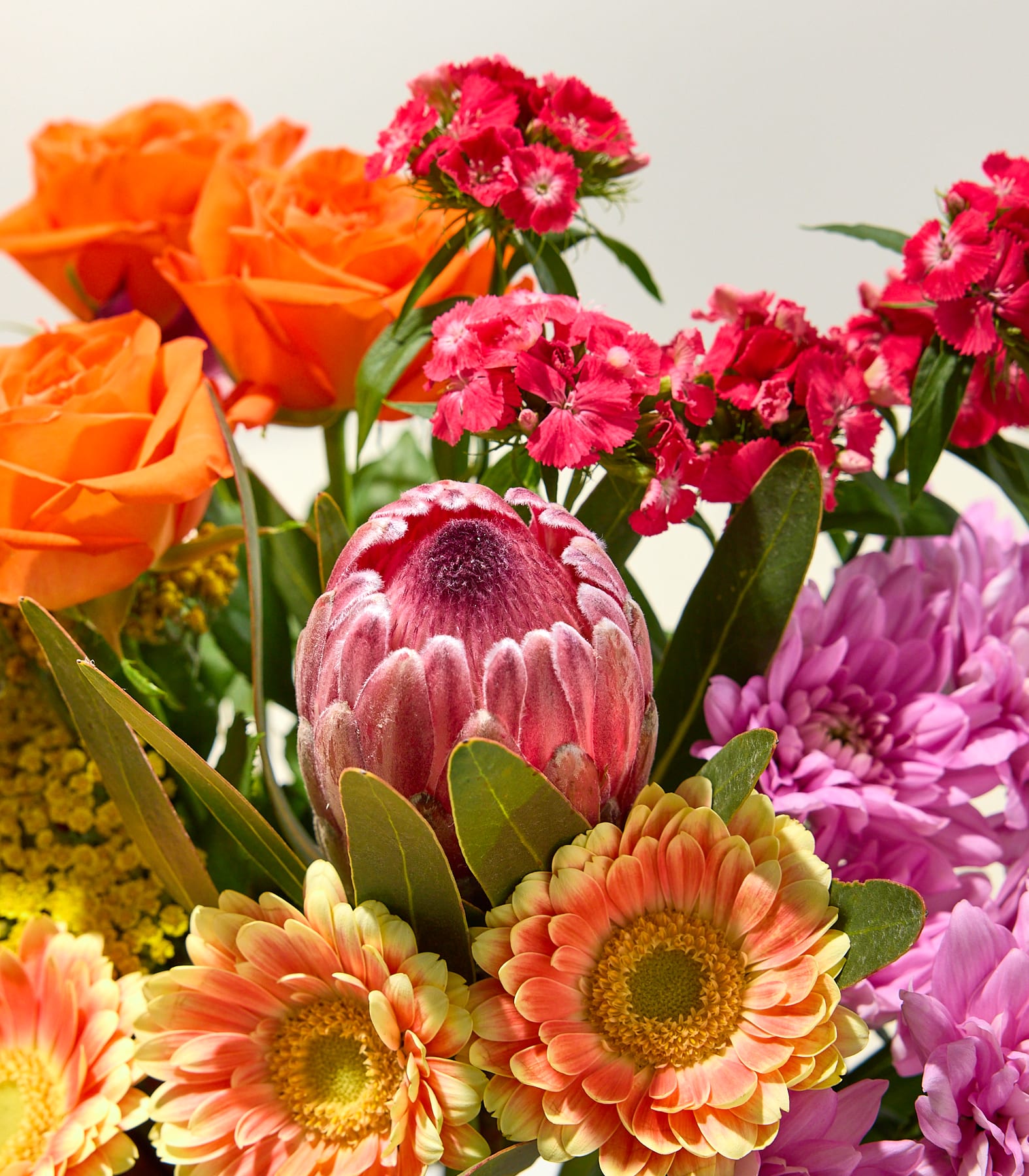 Ein farbenfroher Strauß aus rosa und violetten Blumen, darunter Nelken, Rosen und andere Blüten, vor einem schlichten Hintergrund. (Beschreibungstext KI-generiert)