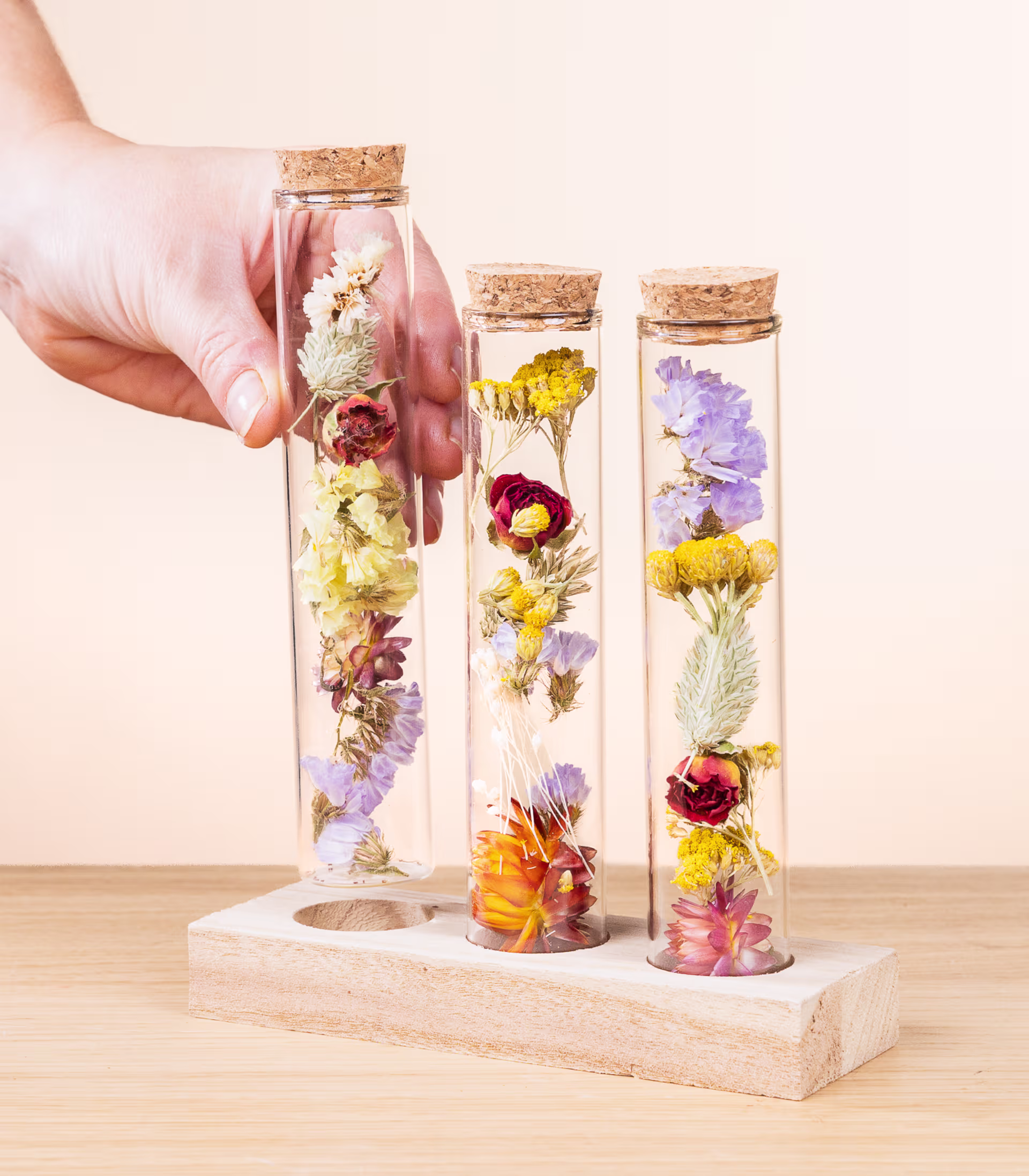 Das Bild zeigt drei Glasgefäße, gefüllt mit verschiedenen getrockneten Blumen und Pflanzen, arrangiert auf einer Holzoberfläche vor einem hellen Hintergrund. (Beschreibungstext KI-generiert)