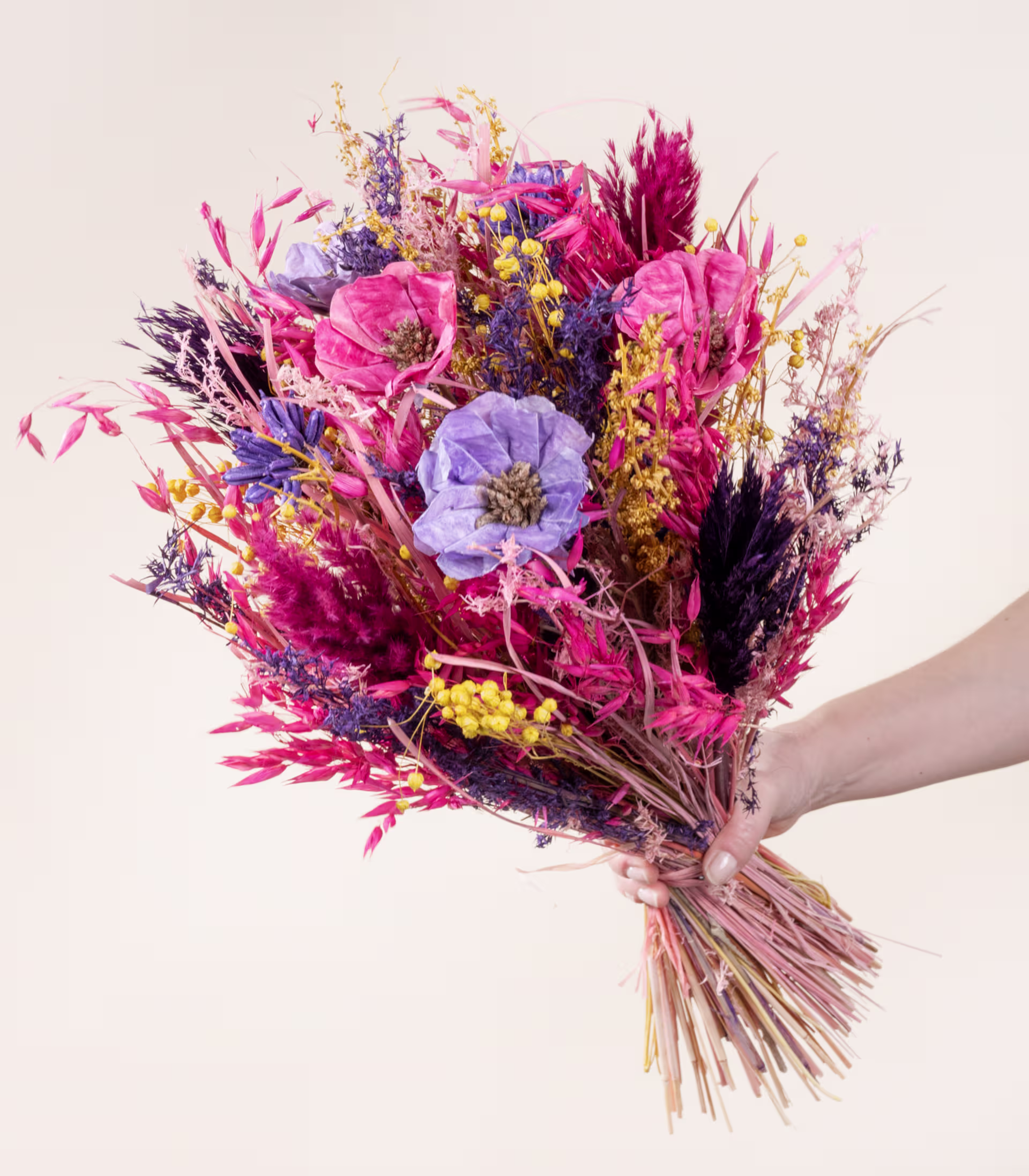 Ein lebendiger Strauß bunter Trockenblumen, darunter rosa, violette und gelbe Blüten, in der Hand gehalten vor einem schlichten, hellen Hintergrund. (Beschreibungstext KI-generiert)