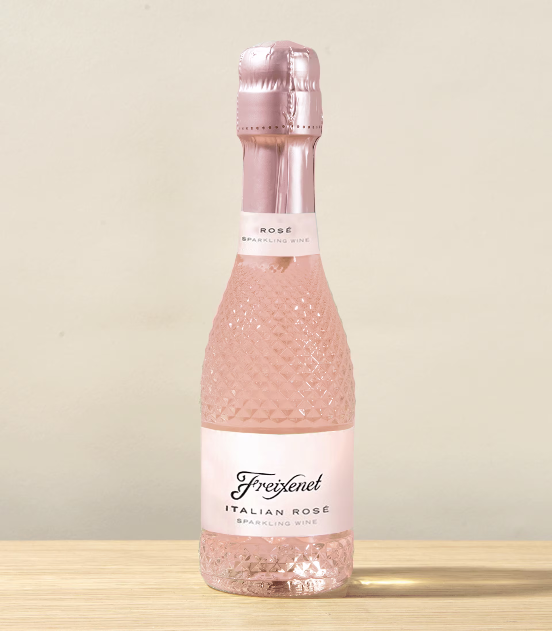 Eine rosafarbene, prickelnde Flasche italienischen Roséweins steht auf einer Holzoberfläche vor einem hellen Hintergrund. (Beschreibungstext KI-generiert)