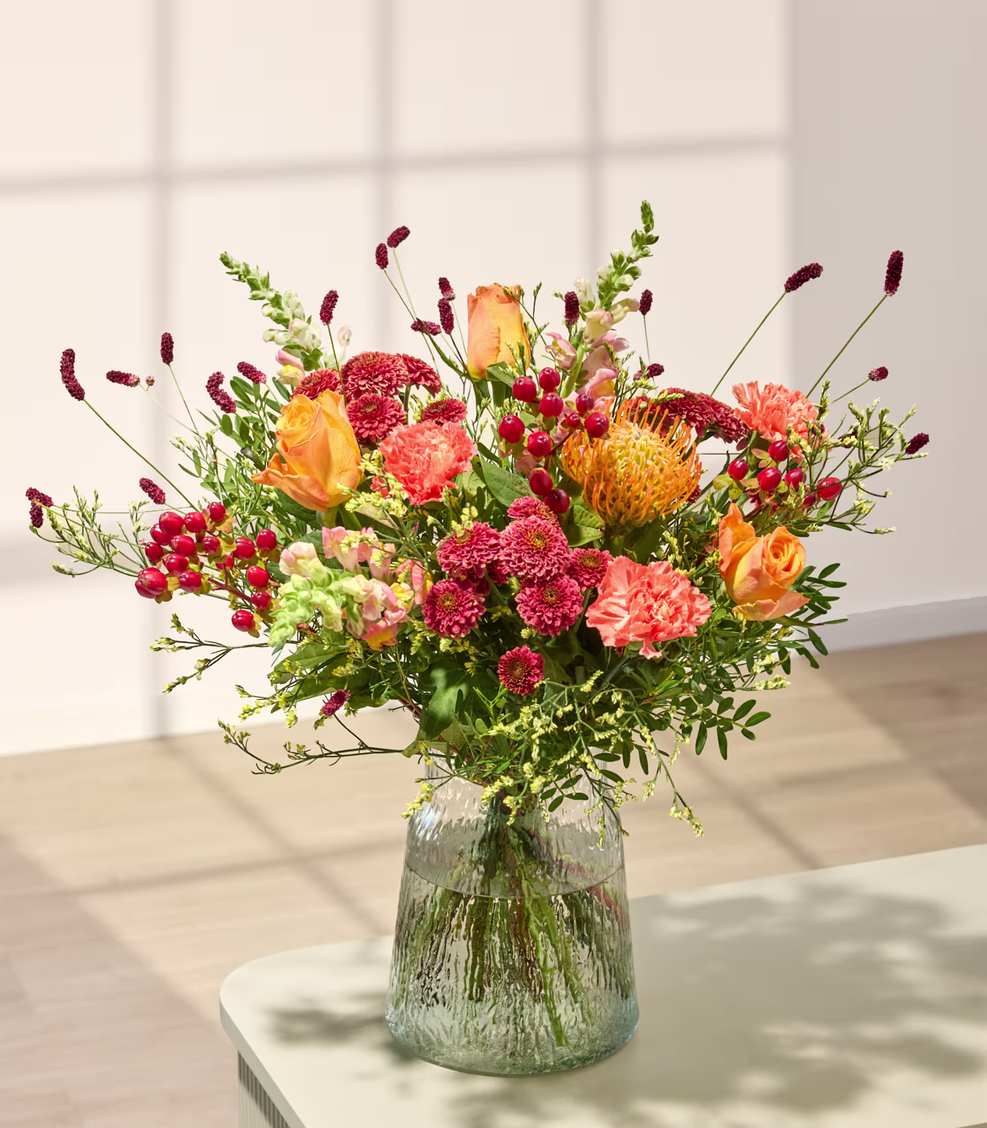 Eine Person in einem weinroten Hemd und Jeans hält einen leuchtenden Strauß orangefarbener und rosafarbener Blumen vor einem schlichten, hellen Hintergrund. (Beschreibungstext KI-generiert)