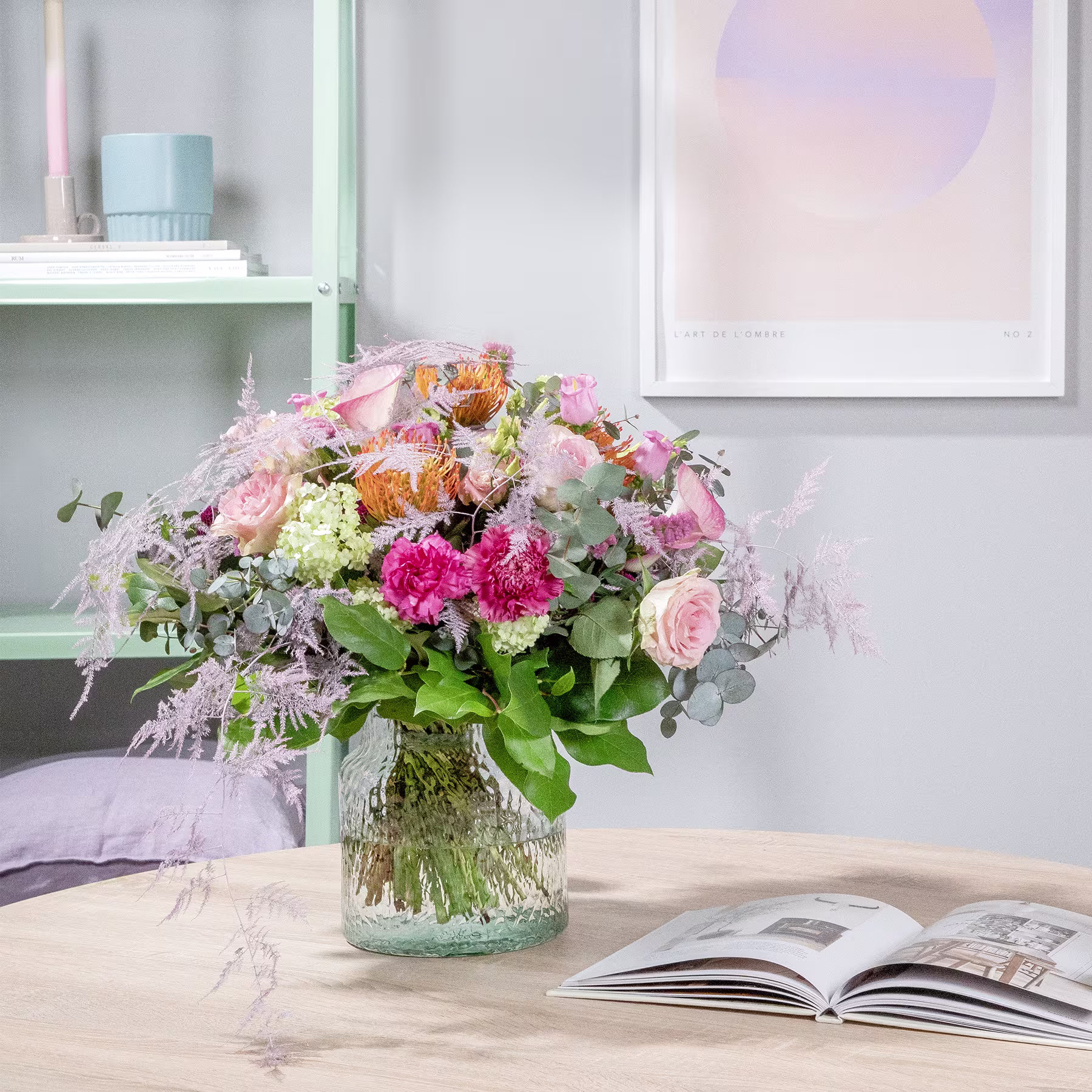 Ein farbenfroher Strauß rosa, gelber und weißer Blumen steht auf einem Holztisch vor einem großen Fenster, im Hintergrund sind ein Buch und andere Dekorationsgegenstände zu sehen. (Beschreibungstext KI-generiert)