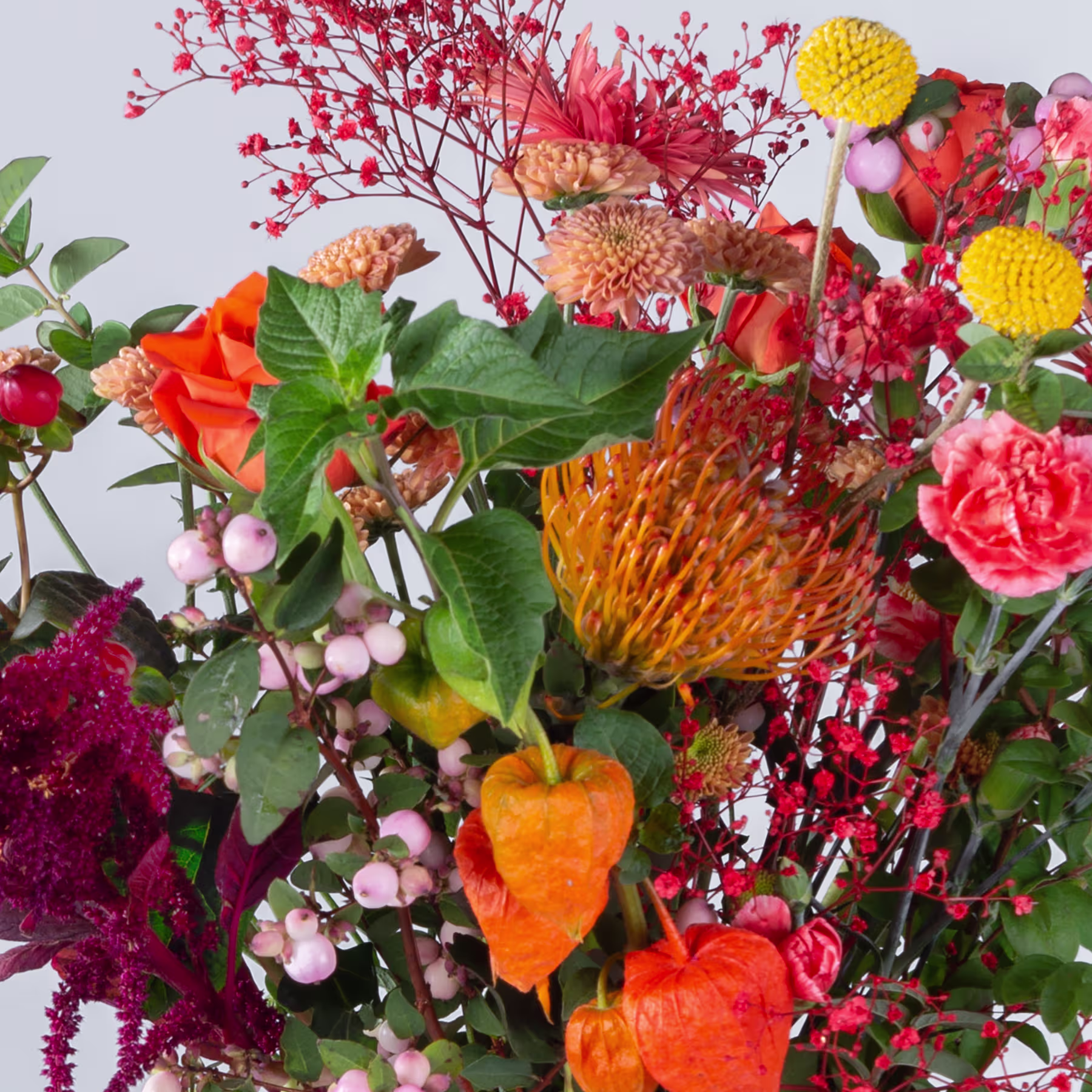 Ein lebendiges und farbenfrohes Arrangement verschiedener Blumen, darunter rote Beeren, gelbe, pomponartige Blüten und orangefarbene, glockenförmige Blüten vor einem hellen Hintergrund. (Beschreibungstext KI-generiert)