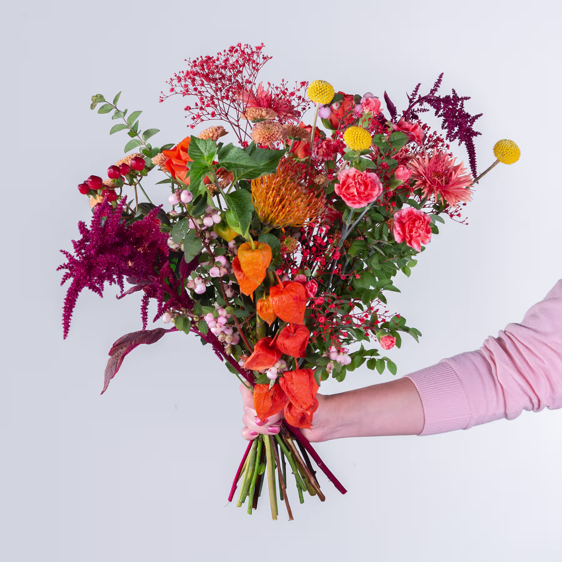 Ein leuchtender Strauß verschiedener bunter Blumen, darunter Rosen, Chrysanthemen und andere Blüten, den eine Person vor einem schlichten Hintergrund in den Händen hält. (Beschreibungstext KI-generiert)