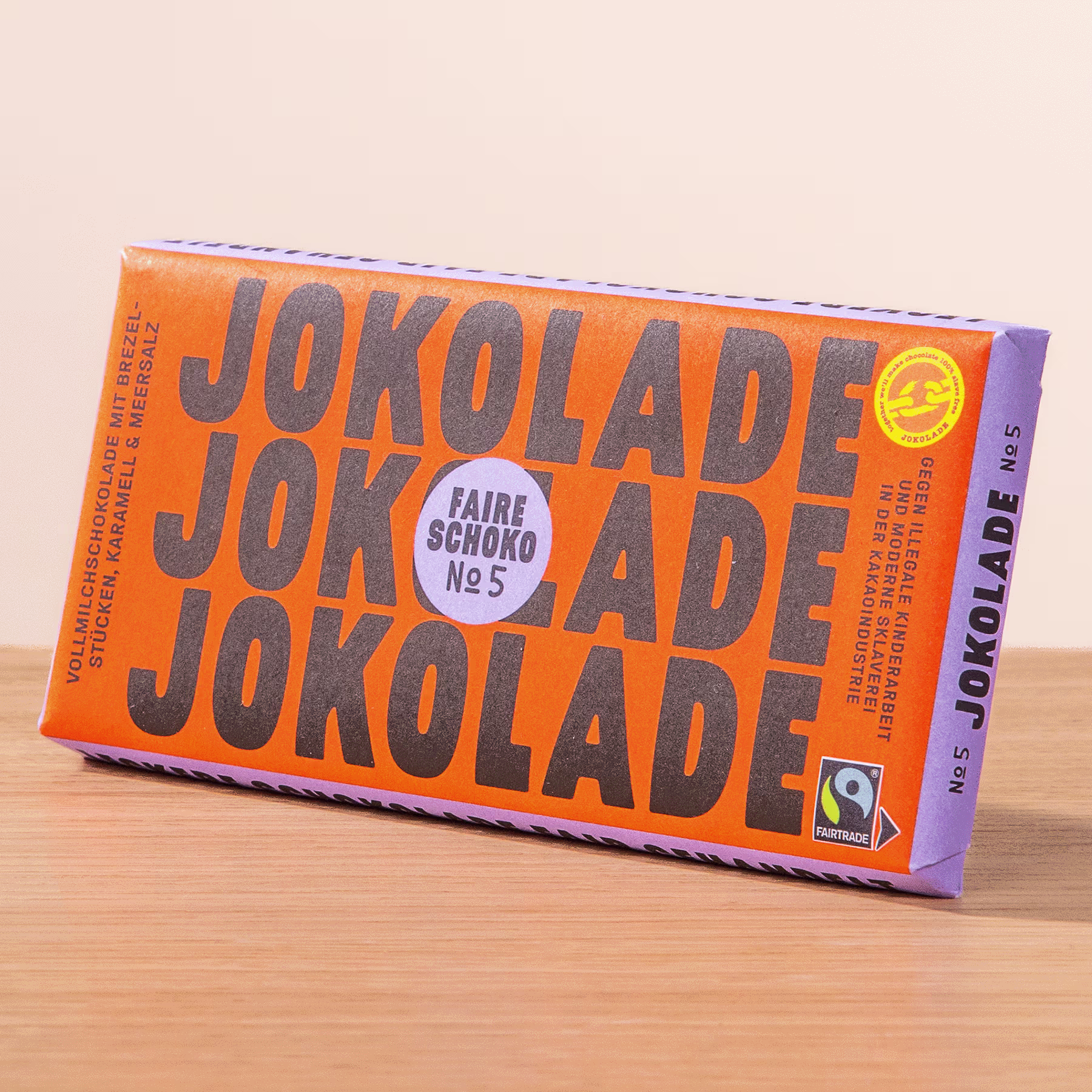 Eine leuchtend orangefarbene Schokoriegelpackung mit dem deutlich sichtbaren Text „JOKOLADE JOKOLADE JOKOLADE“ vor einem schlichten Hintergrund. (Beschreibungstext KI-generiert)
