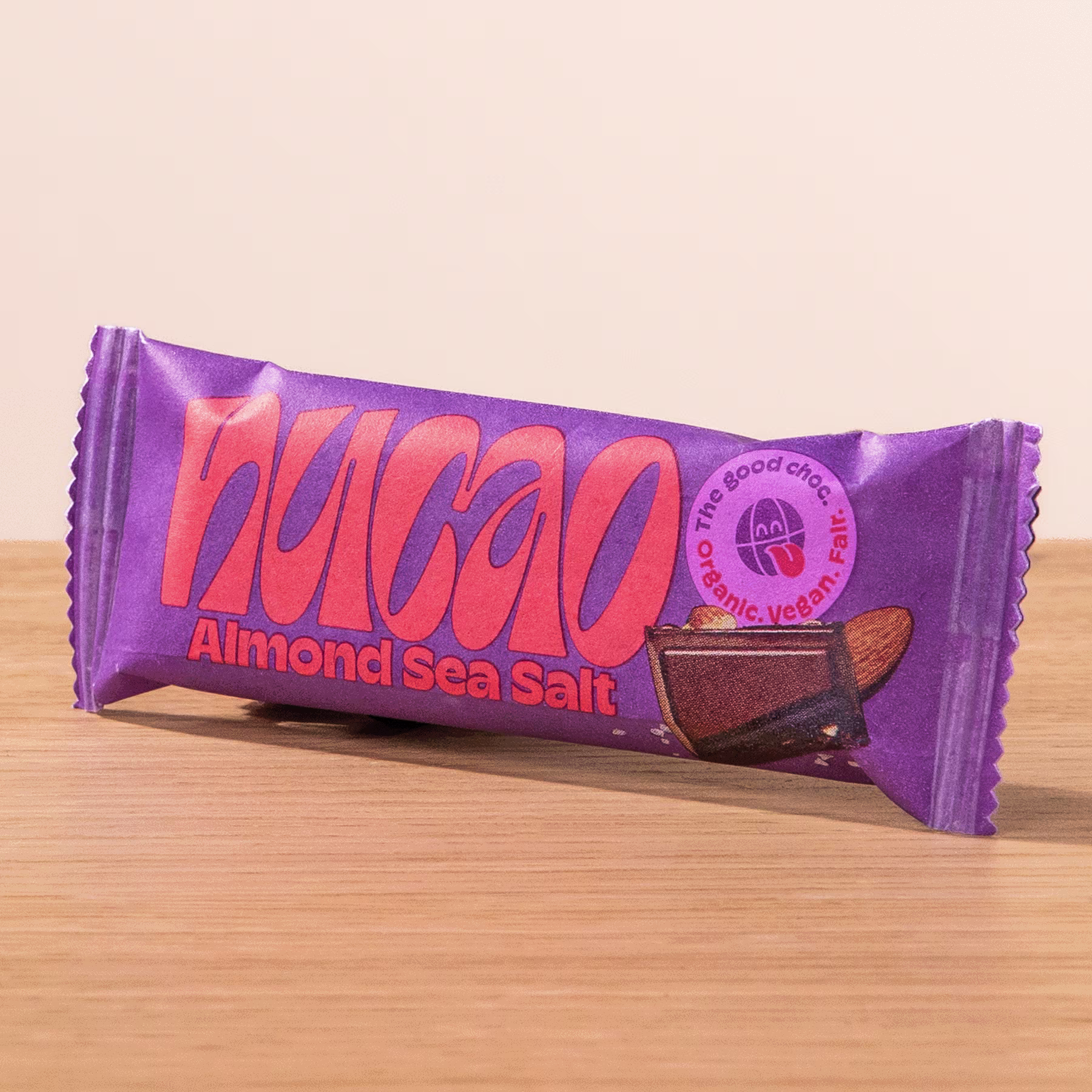 Ein lila verpackter Snackriegel mit dem Wort „Nakao“ und der Geschmacksrichtung „Mandel-Meersalz“, die deutlich sichtbar auf einer Holzoberfläche abgebildet sind. (Beschreibungstext KI-generiert)