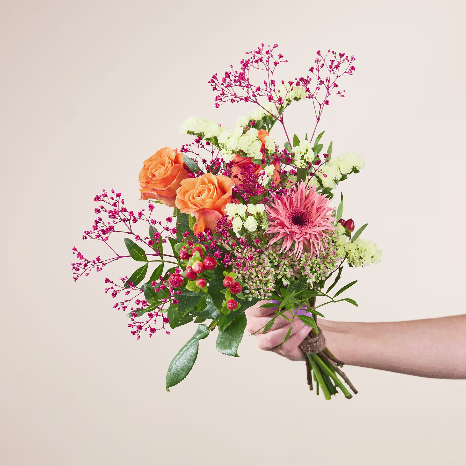 Ein leuchtender Strauß bunter Blumen, darunter orangefarbene Rosen, rosa Gerbera und verschiedene Grünpflanzen, wird vor einem schlichten Hintergrund in den Händen einer Person gehalten. (Beschreibungstext KI-generiert)