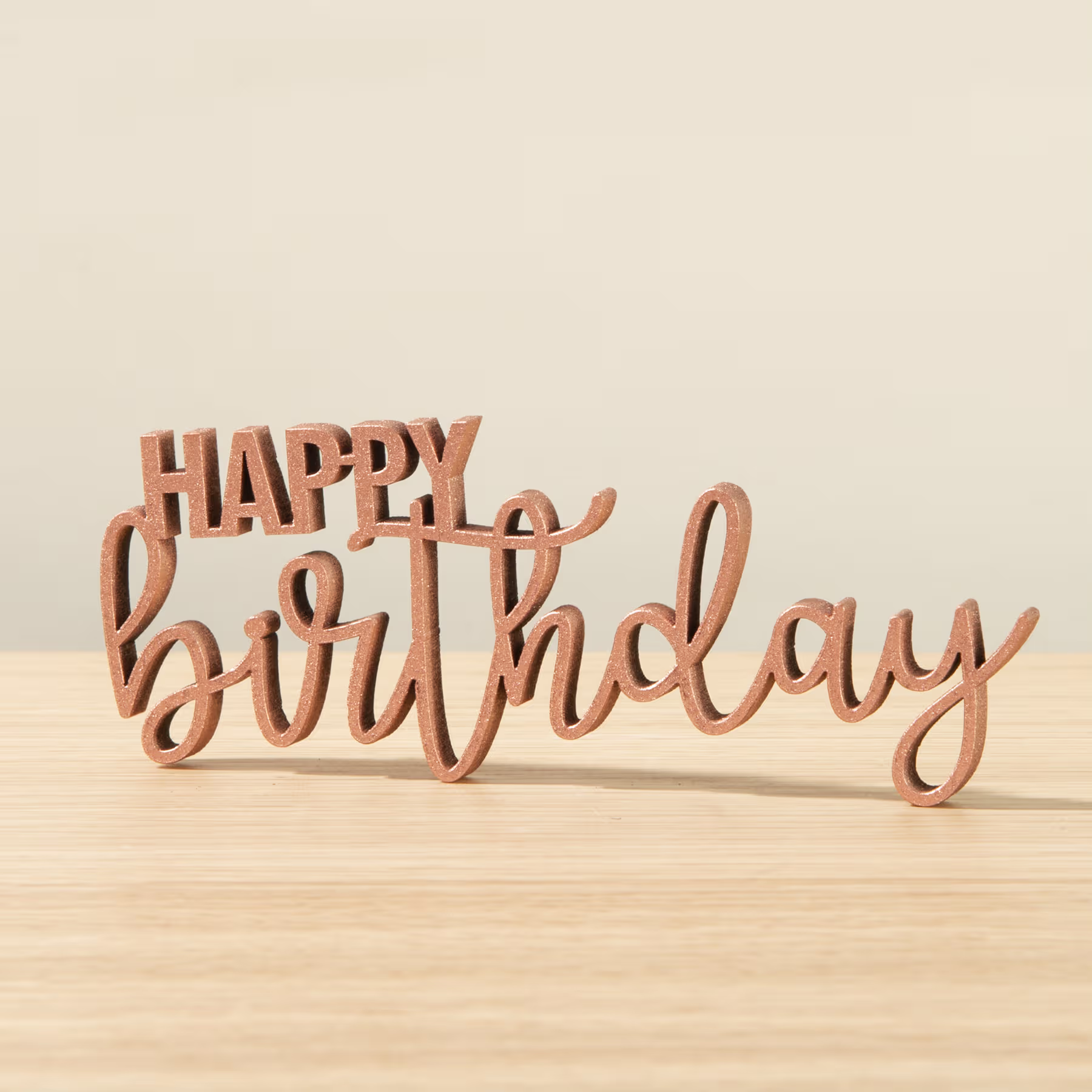Das Bild zeigt den Schriftzug „Happy Birthday“ in Holzbuchstaben auf einer Holzoberfläche vor einem hellen Hintergrund. (Beschreibungstext KI-generiert)