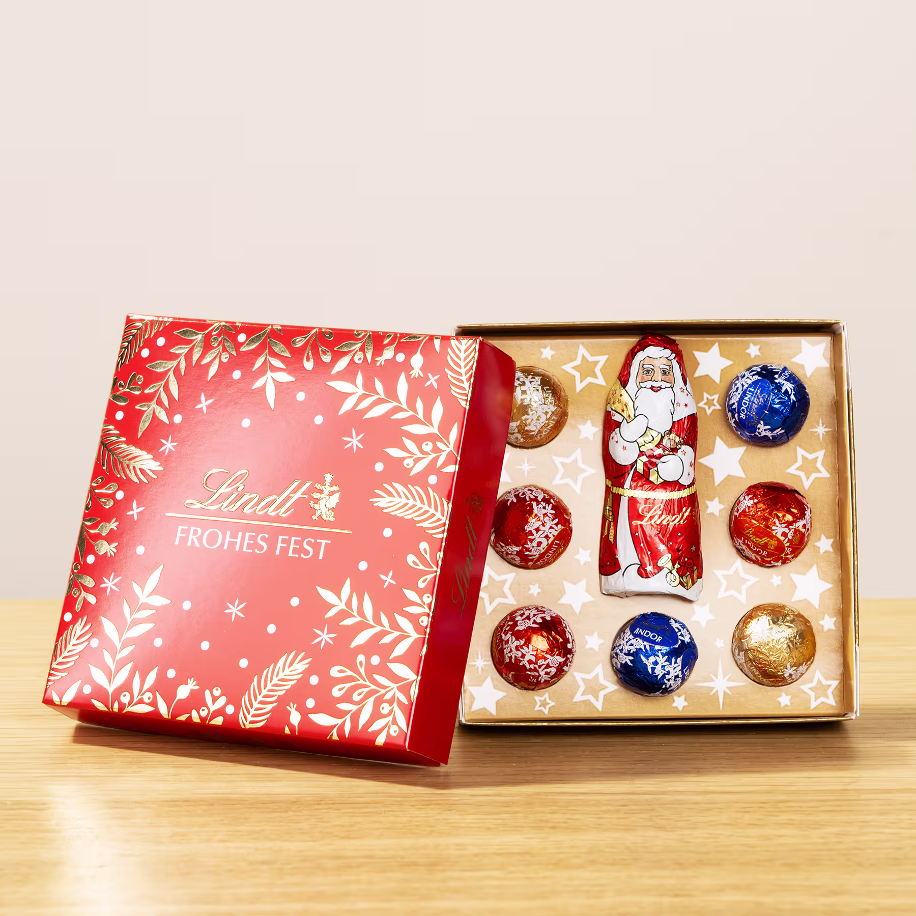 Auf einer Holzoberfläche steht eine rot-weiße Geschenkbox mit verschiedenen weihnachtlichen Schokoladenbonbons und Dekorationen. (Beschreibungstext KI-generiert)