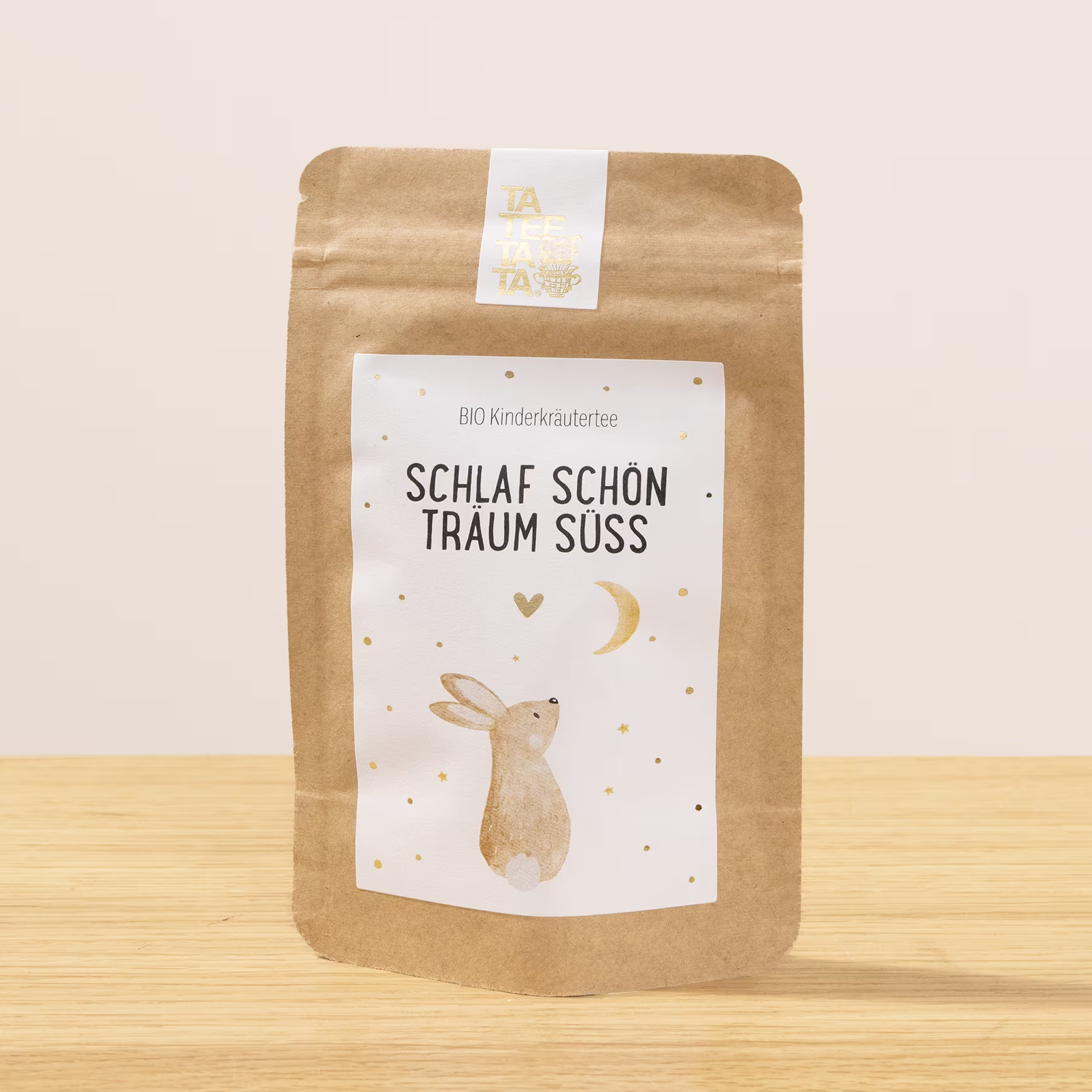 Eine braune Papiertüte mit weißem Etikett, auf dem sich auf einer Holzoberfläche die Illustration eines schlafenden Kaninchens und der Text „Schlaf schon traum suss“ befinden. (Beschreibungstext KI-generiert)