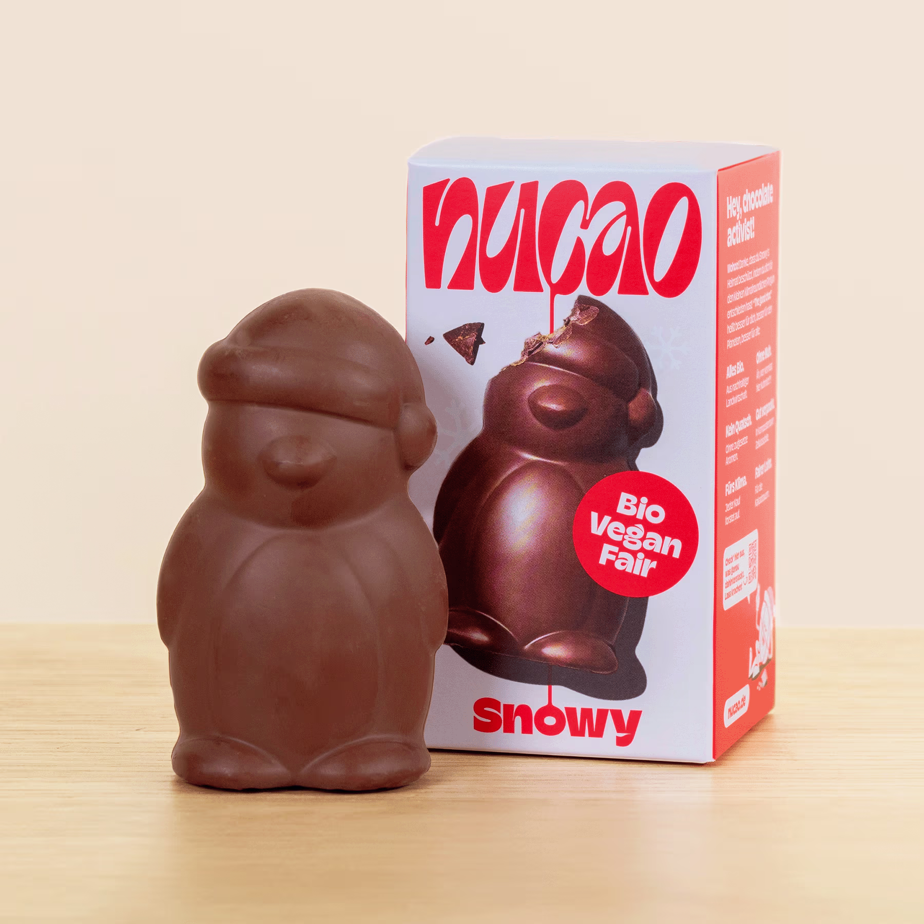 Eine Schokoladenfigur einer Figur, die einem Schneemann oder einer ähnlichen Figur ähnelt, neben einer Schachtel mit der Aufschrift „Vegan Fair“ und „Snowy“. (Beschreibungstext KI-generiert)