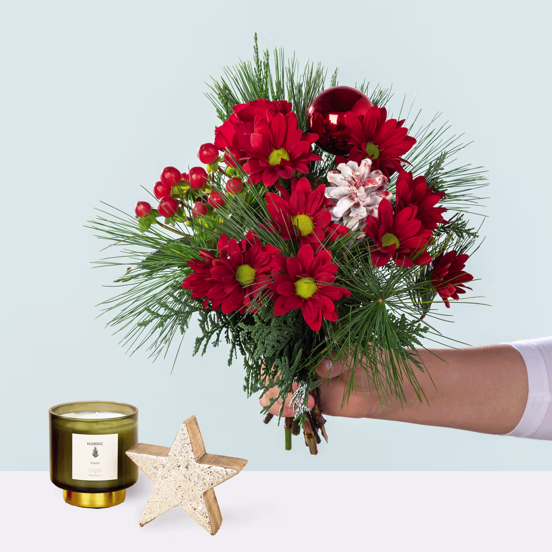 Ein leuchtender Strauß roter und rosa Blumen, darunter Chrysanthemen und Pfingstrosen, in der Hand gehalten vor einem schlichten Hintergrund, begleitet von einer Kerze und einem Seestern. (Beschreibungstext KI-generiert)