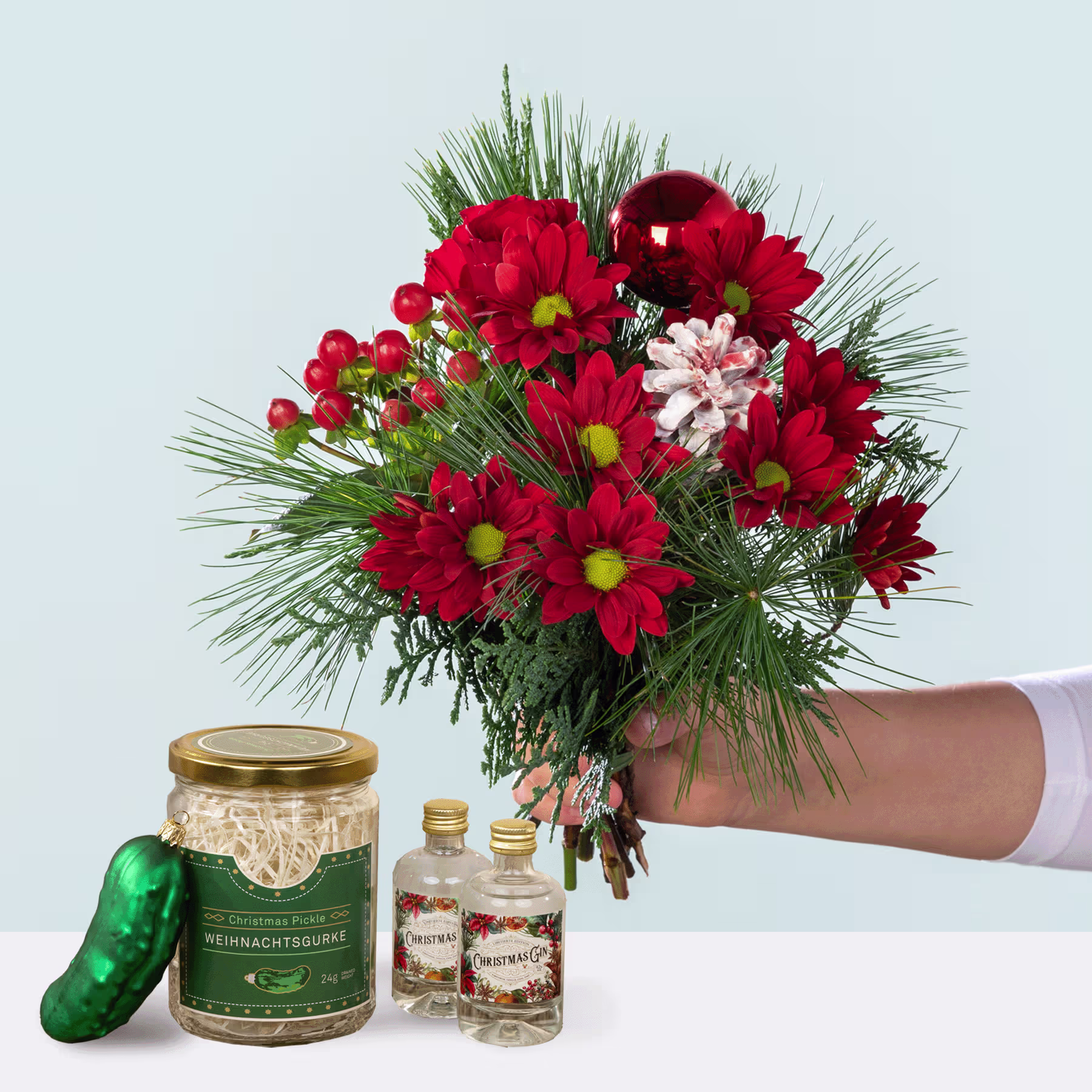 Ein farbenfroher Strauß roter und rosa Blumen, darunter Chrysanthemen und andere Blüten, wird neben einem Glas mit eingelegtem Gemüse und zwei kleinen Flaschen präsentiert, alles vor einem schlichten Hintergrund. (Beschreibungstext KI-generiert)