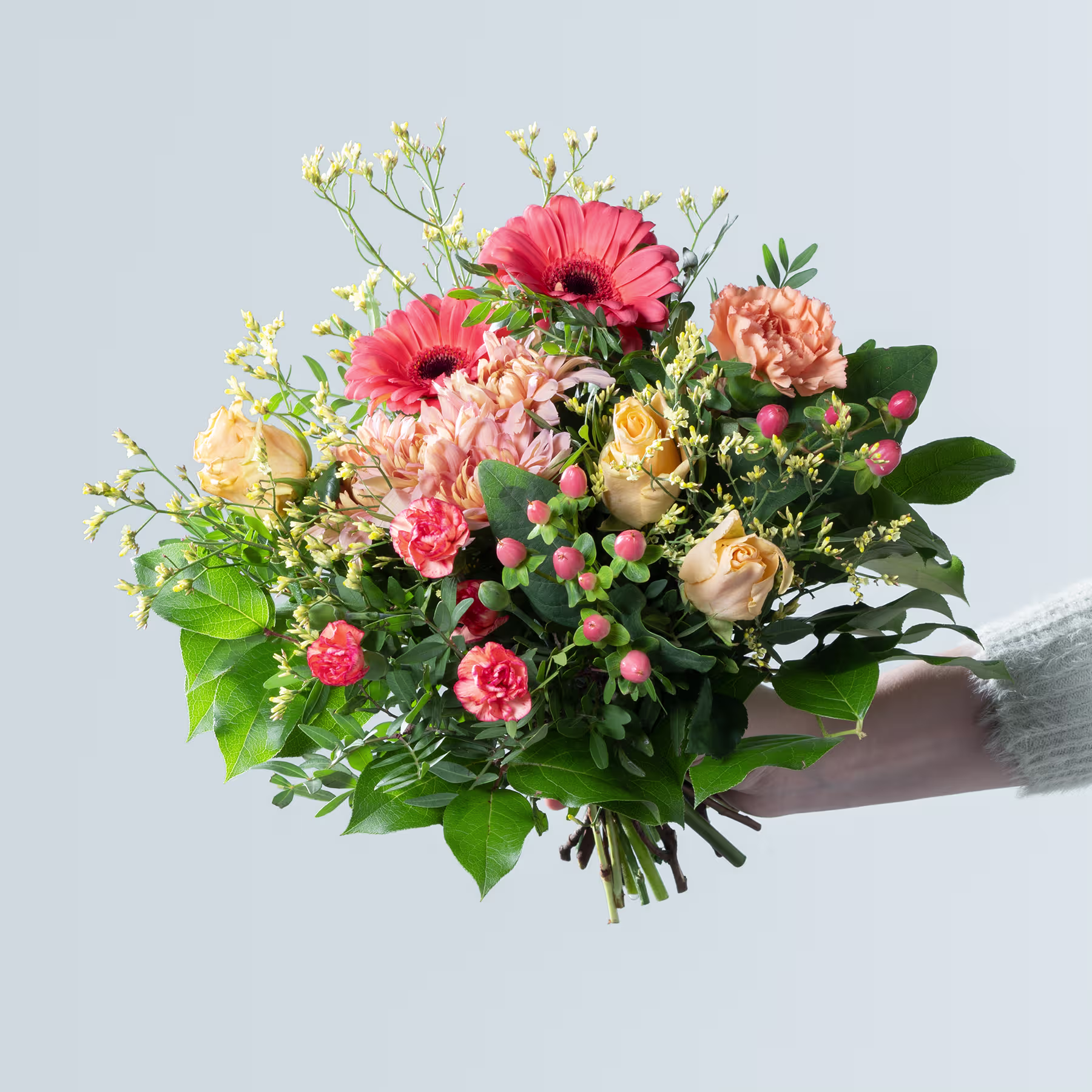 Ein lebendiger Strauß bunter Blumen, darunter rosa Gerbera, pfirsichfarbene Rosen und verschiedene Grünpflanzen, wird vor einem schlichten Hintergrund in den Händen einer Person gehalten. (Beschreibungstext KI-generiert)