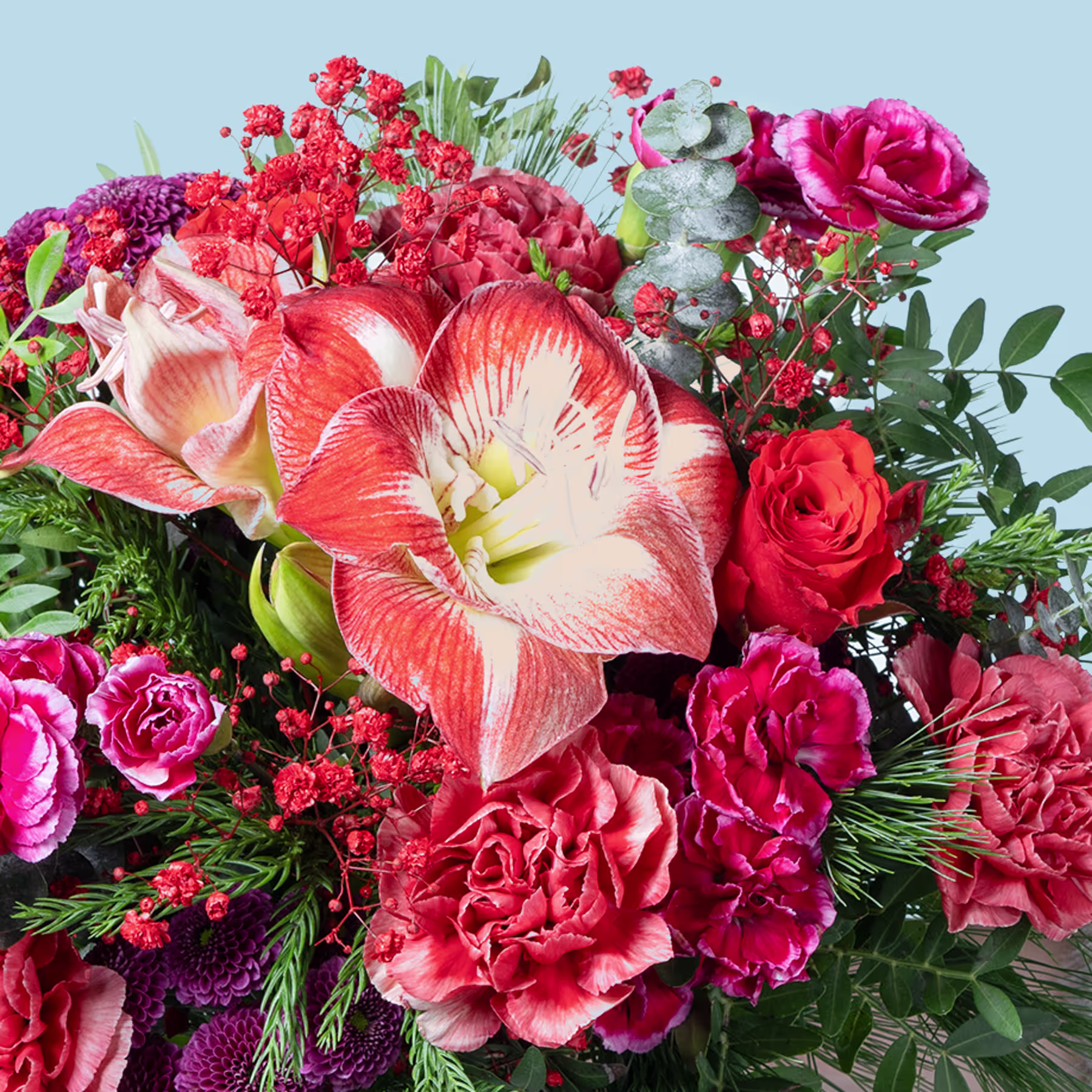 Ein leuchtender Strauß roter, rosa und orangefarbener Blumen, darunter Rosen, Nelken und eine Amaryllis, vor dem Hintergrund eines klaren blauen Himmels. (Beschreibungstext KI-generiert)