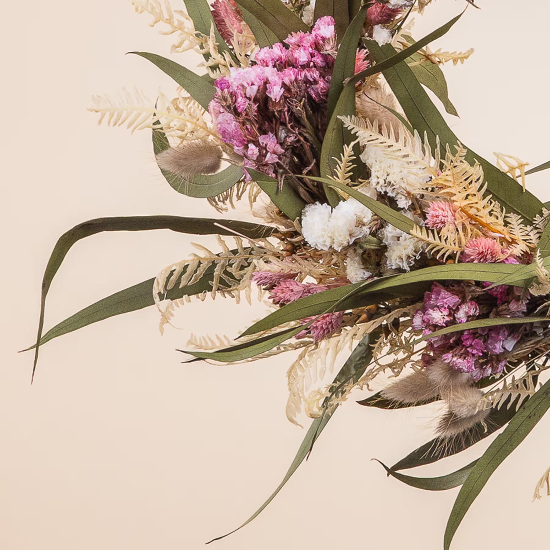 Ein farbenfroher Blumenkranz aus verschiedenen Blüten und Grünpflanzen wird von den Händen einer Person vor einem schlichten Hintergrund gehalten. (Beschreibungstext KI-generiert)