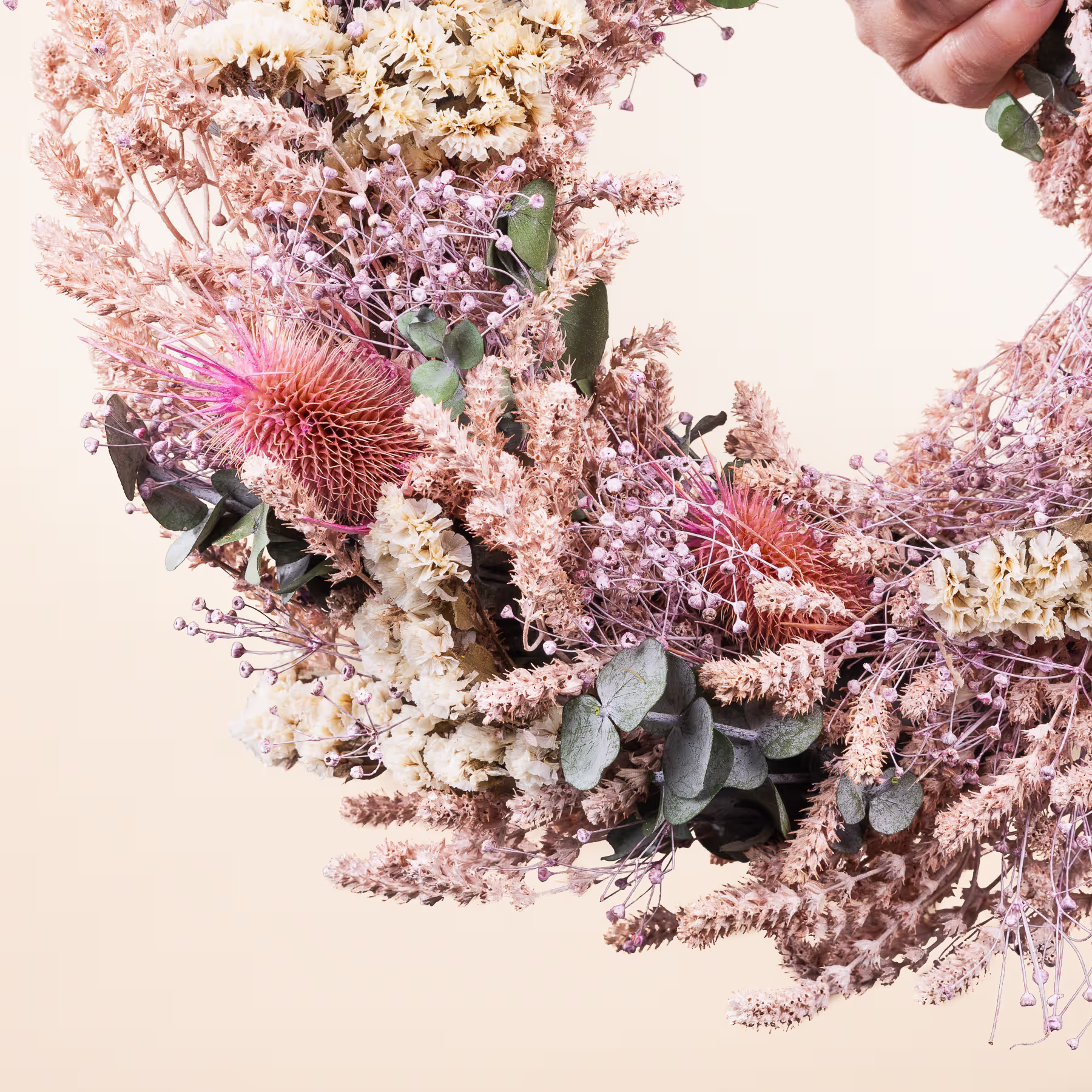 Ein lebendiger Strauß verschiedener Blumen, darunter rosa Proteablüten, zarte weiße und violette Blüten und üppiges Grün, arrangiert in einer optisch ansprechenden Komposition vor einem weichen, neutralen Hintergrund. (Beschreibungstext KI-generiert)