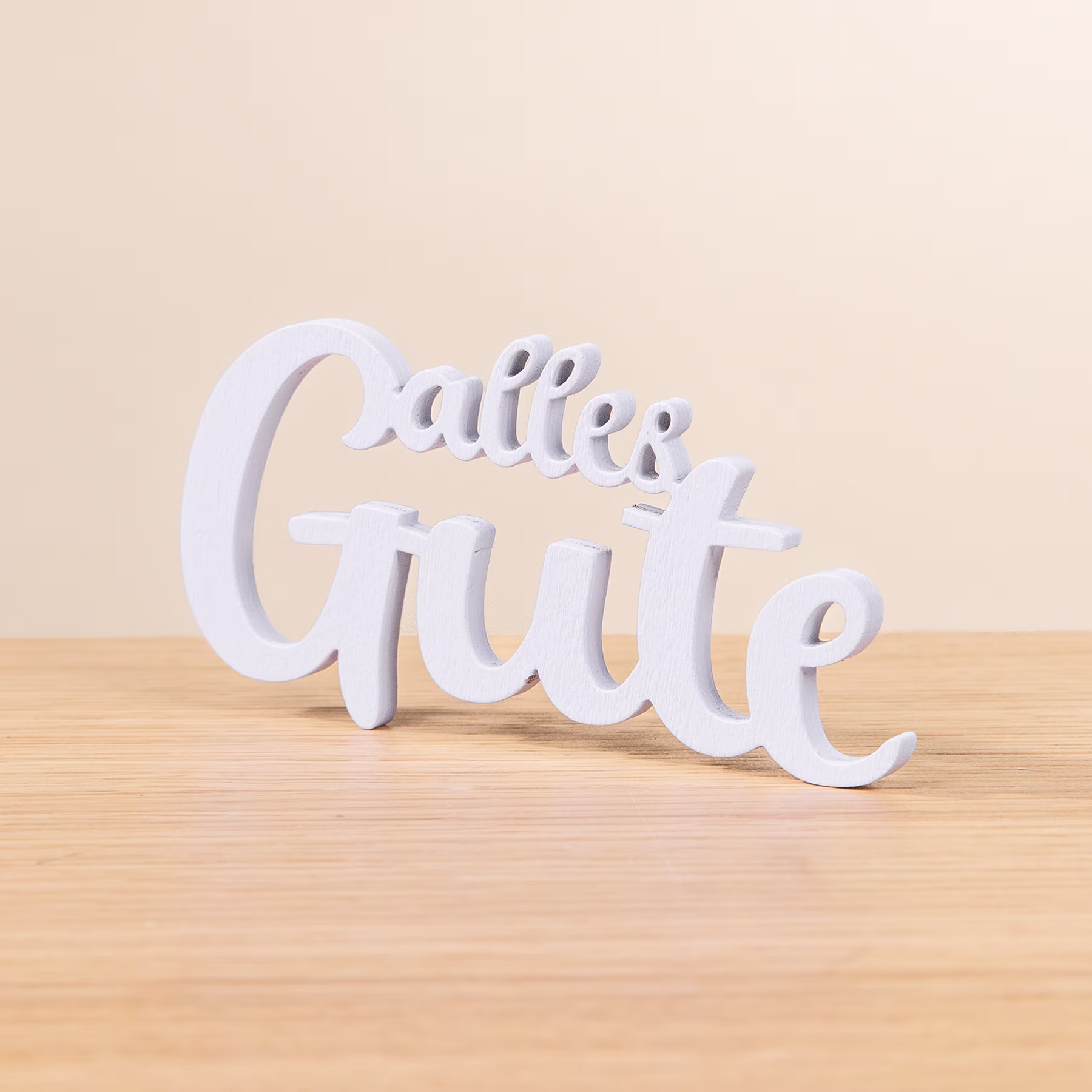 Das Bild zeigt den Schriftzug „Callie Gute“ in weißen, dreidimensionalen Buchstaben auf einer Holzoberfläche mit hellem Hintergrund. (Beschreibungstext KI-generiert)