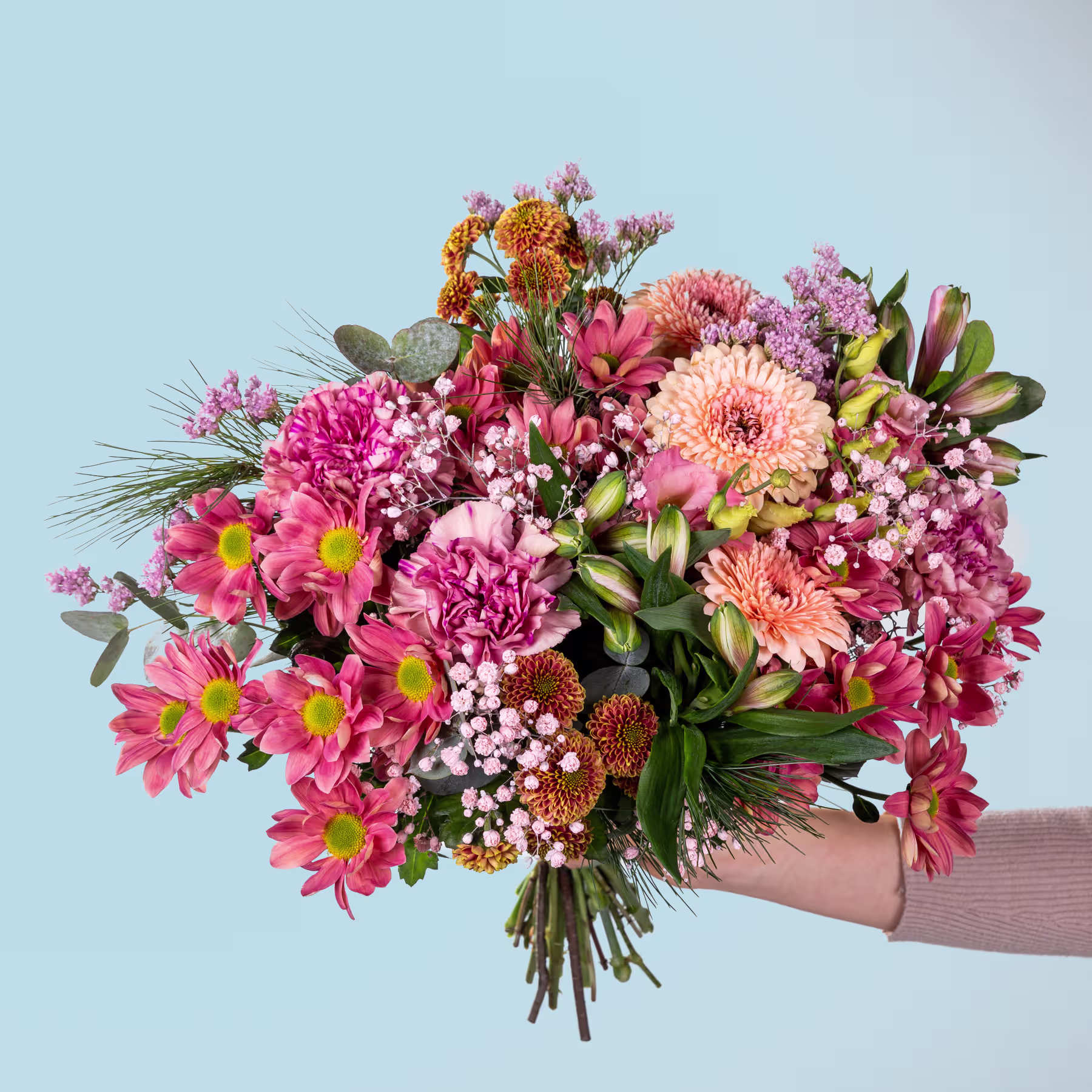 Ein farbenfroher Strauß verschiedener rosa, orangefarbener und gelber Blumen, darunter Dahlien, Chrysanthemen und andere Blüten, die eine Person vor einem schlichten blauen Hintergrund in den Händen hält. (Beschreibungstext KI-generiert)