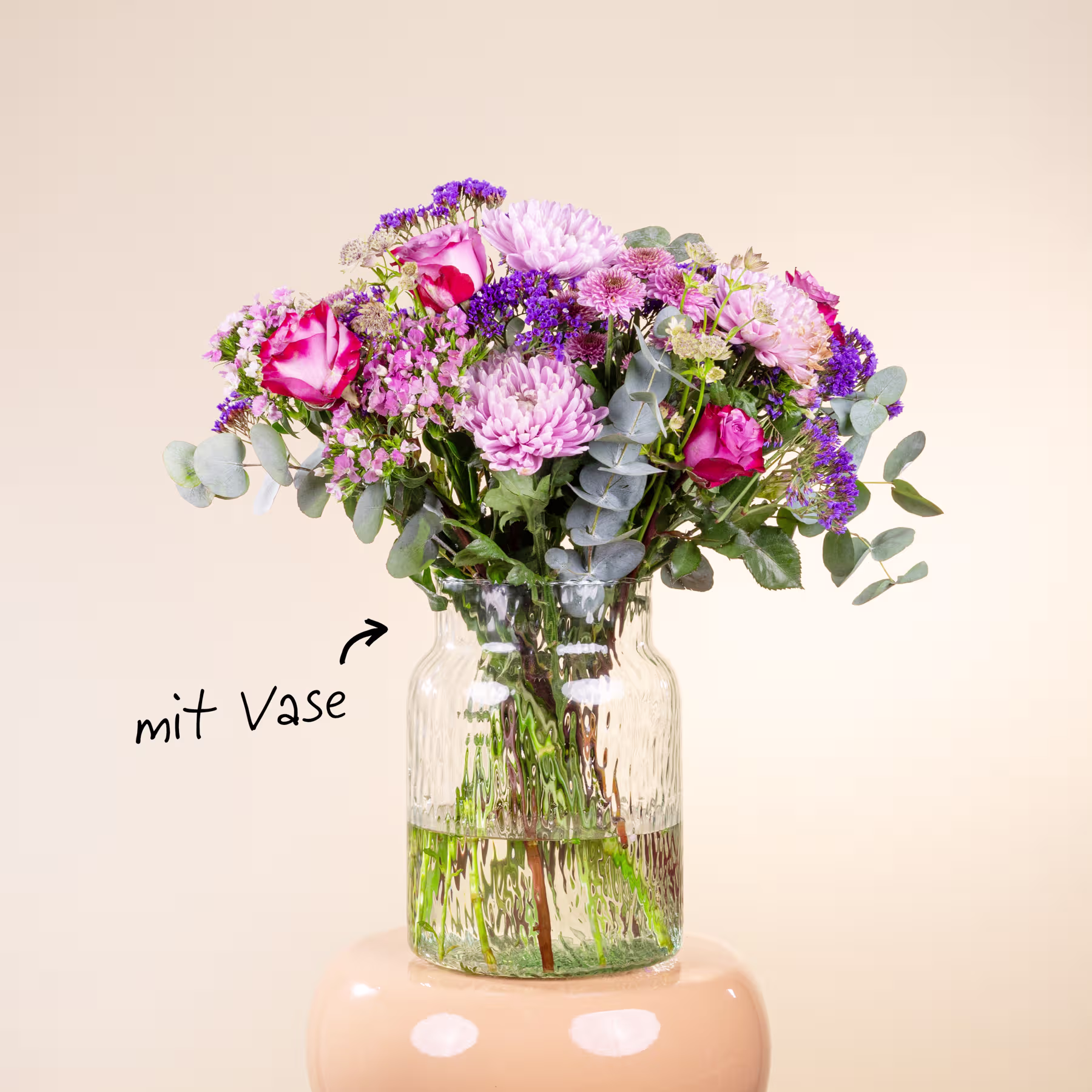 Ein lebendiger Strauß verschiedener bunter Blumen, darunter rosa Rosen, violette Astern und grünes Laub, wird in einer Glasvase vor einem schlichten, hellen Hintergrund präsentiert. (Beschreibungstext KI-generiert)