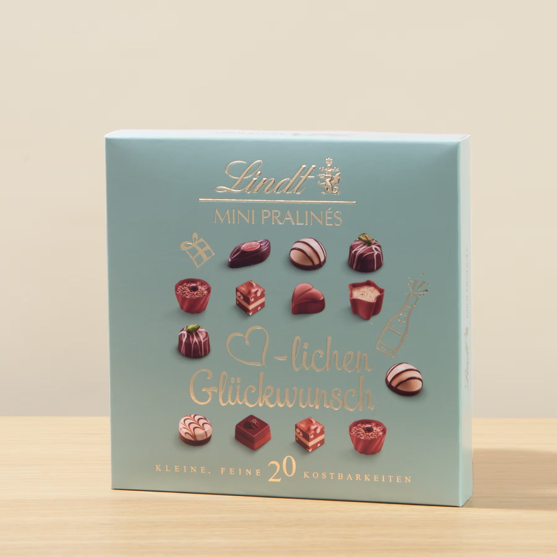 Eine blaue Schachtel mit verschiedenen Schokoladenpralinen, auf deren Vorderseite die Aufschrift „Mini Pralines“ und „Herzlichen Glückwunsch“ aufgedruckt ist. (Beschreibungstext KI-generiert)