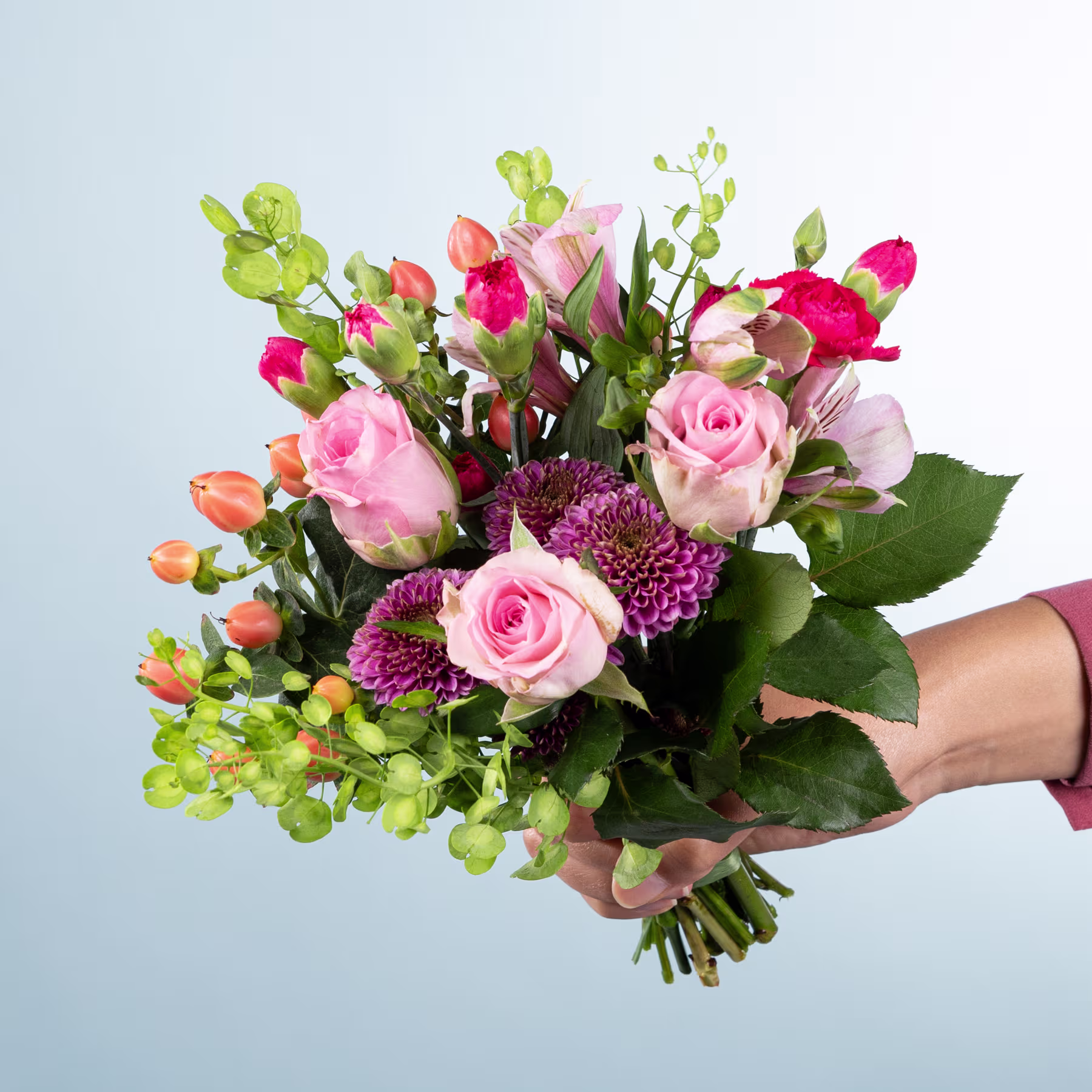 Ein leuchtender Strauß aus rosa Rosen, grünem Laub und anderen bunten Blumen, den eine Person vor einem schlichten hellblauen Hintergrund in den Händen hält. (Beschreibungstext KI-generiert)