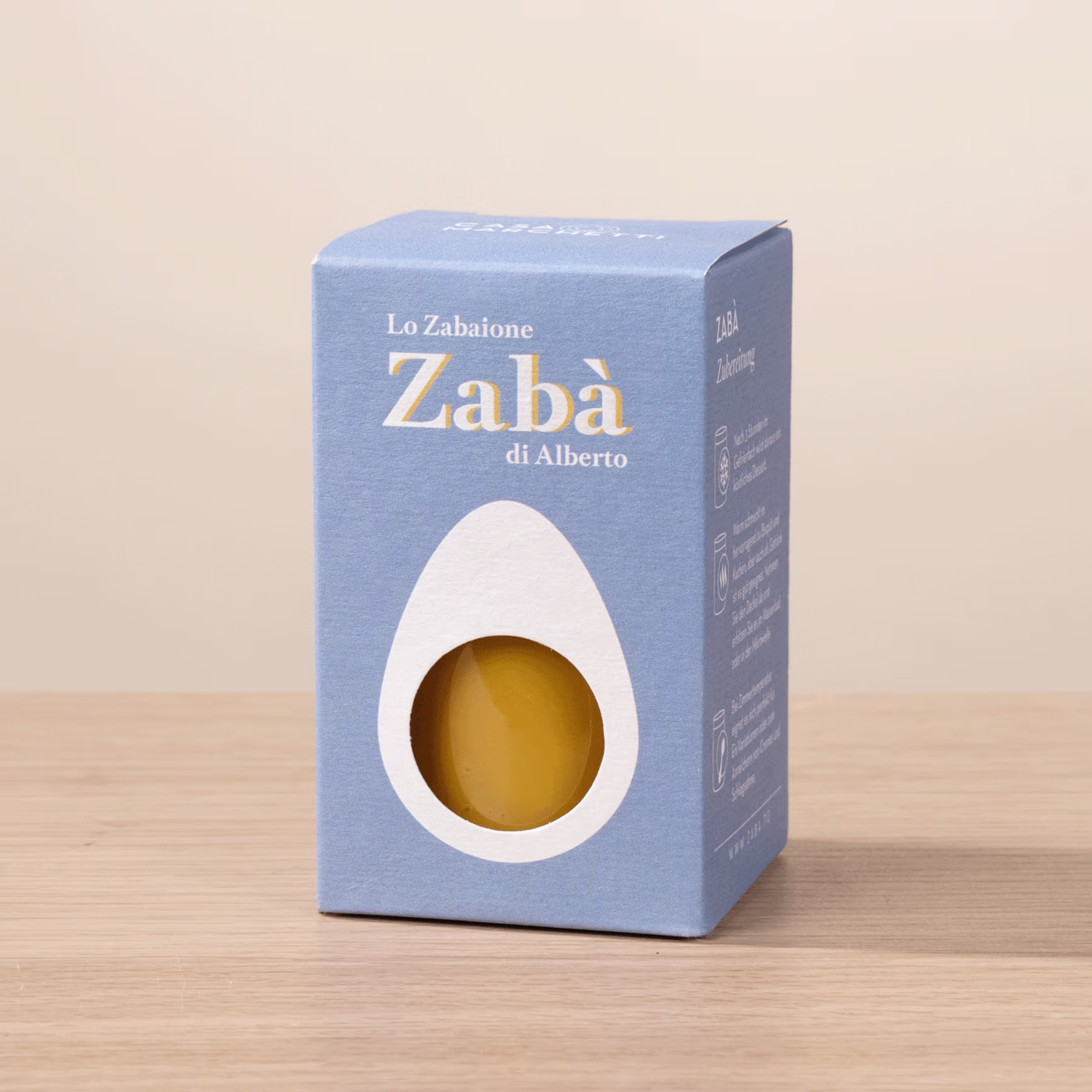 Auf einer Holzoberfläche steht eine blaue Schachtel mit dem Text „Lo Zabalone Zaba di Alberto“ und enthält einen gelben Gegenstand. (Beschreibungstext KI-generiert)